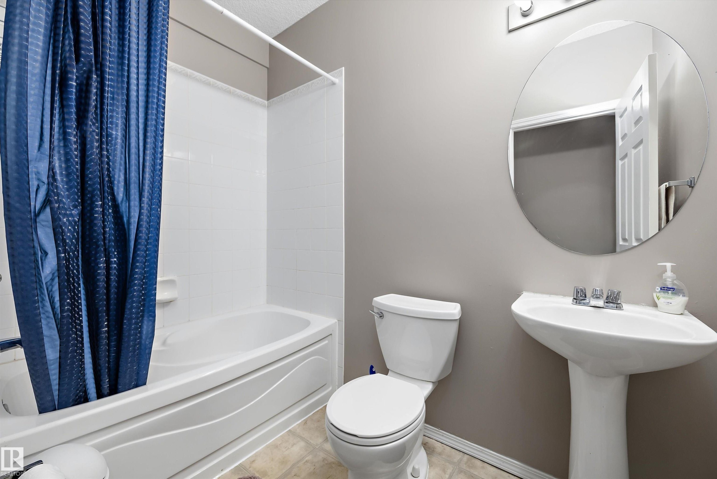 White pedestal sink with chrome faucet, circular wall mirror, and white toilet - 3114 32 Avenue Nw, Edmonton, AB