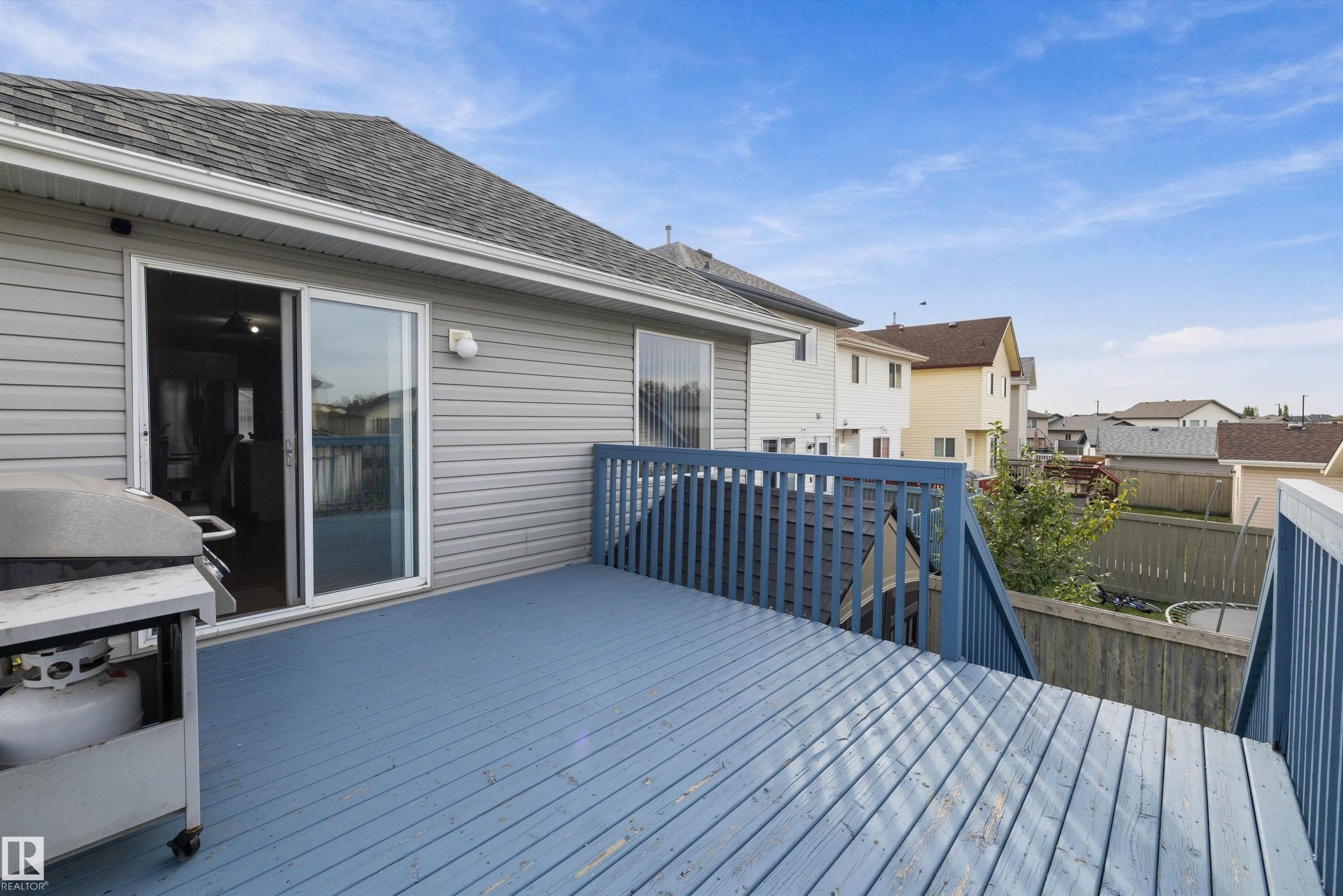 Spacious wood deck with blue finish, full-height railing, and sliding glass door access - 3114 32 Avenue Nw, Edmonton, AB