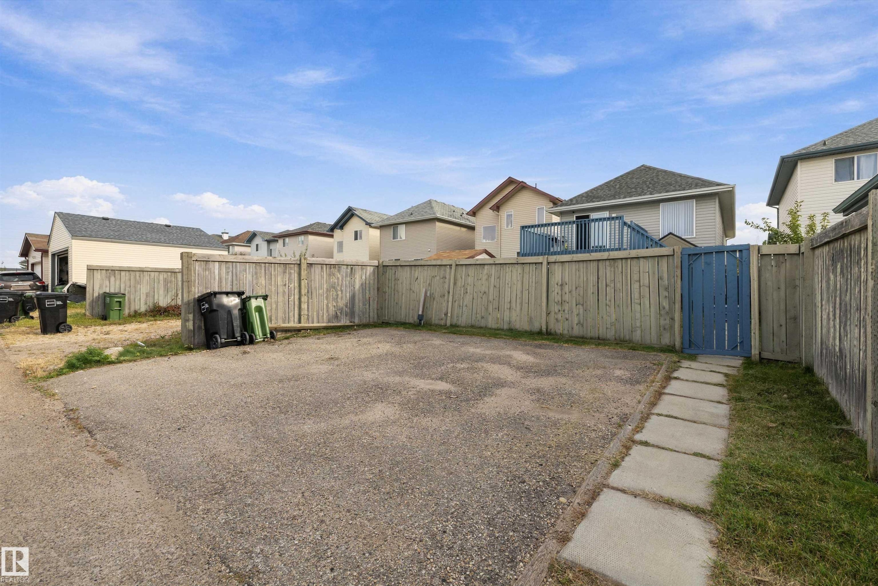 Gravel parking area featuring a privacy fence and a paved walkway with a blue gate - 3114 32 Avenue Nw, Edmonton, AB