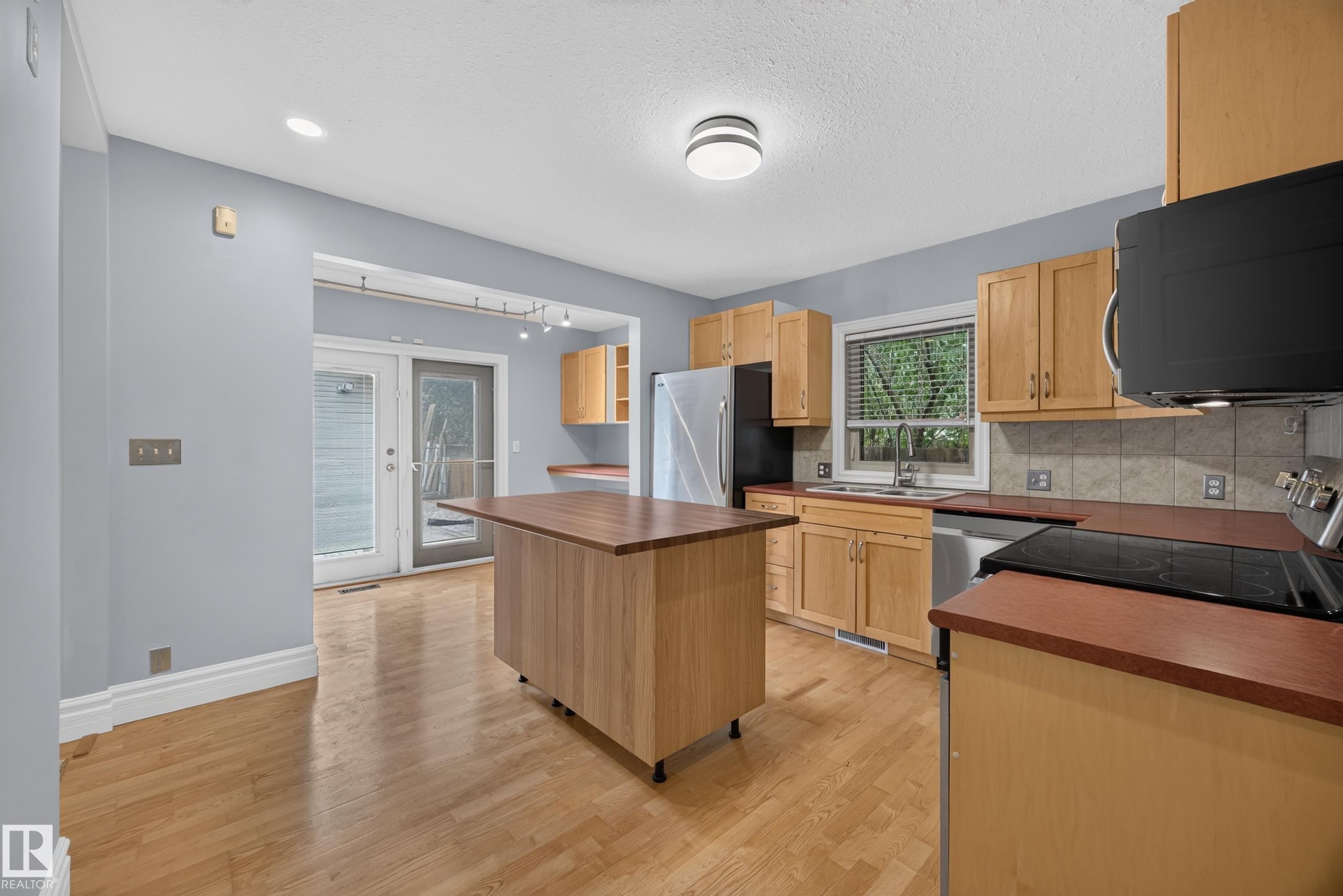 Kitchen featuring wood-finish flooring, natural wood cabinetry, a movable island with wood-finish countertop, stainless steel appliances, and double glass doors - 9615 75 Avenue Nw, Edmonton, AB