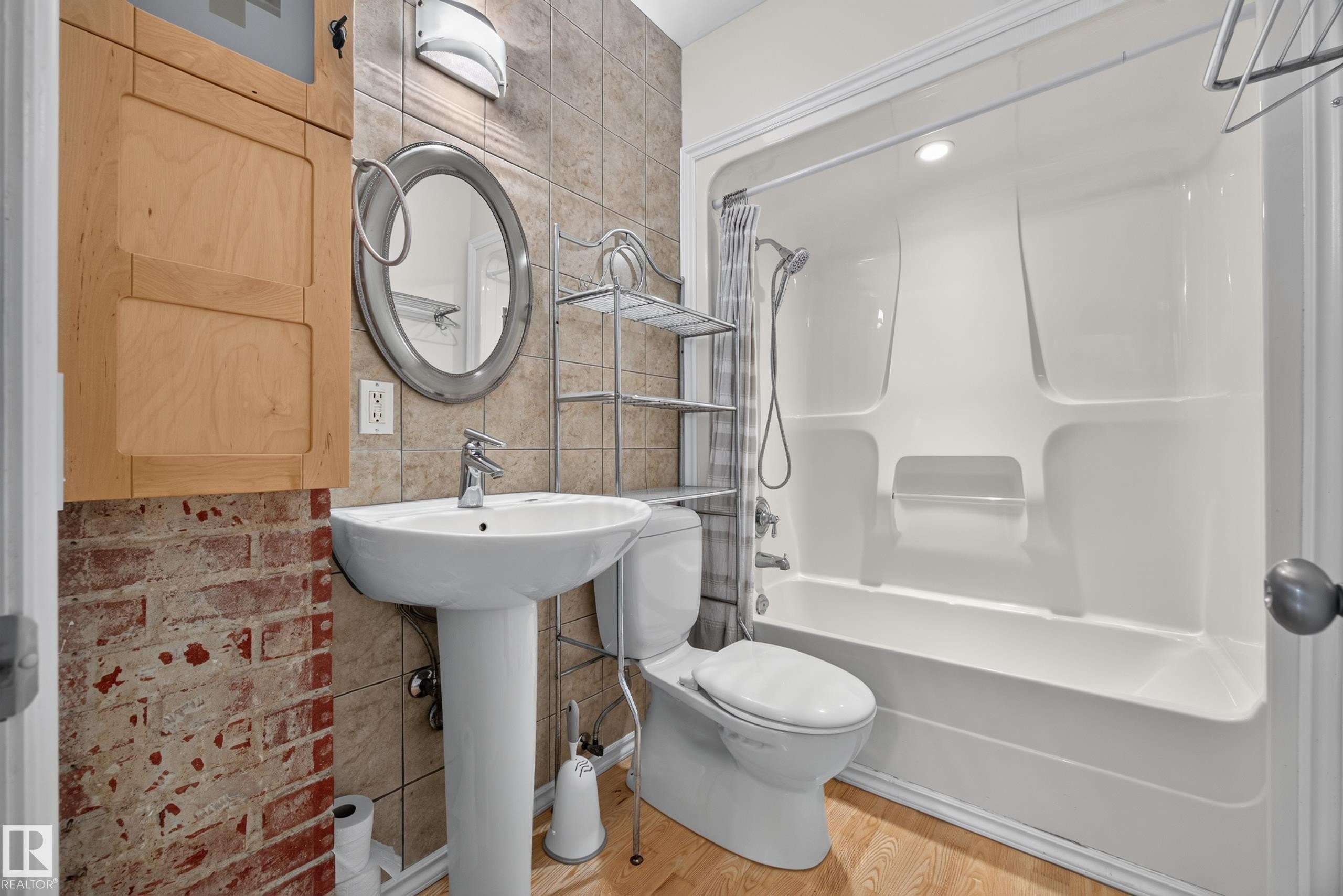 Pedestal sink with chrome faucet, tub/shower combination, decorative wall tile, and wood-finish flooring - 9615 75 Avenue Nw, Edmonton, AB