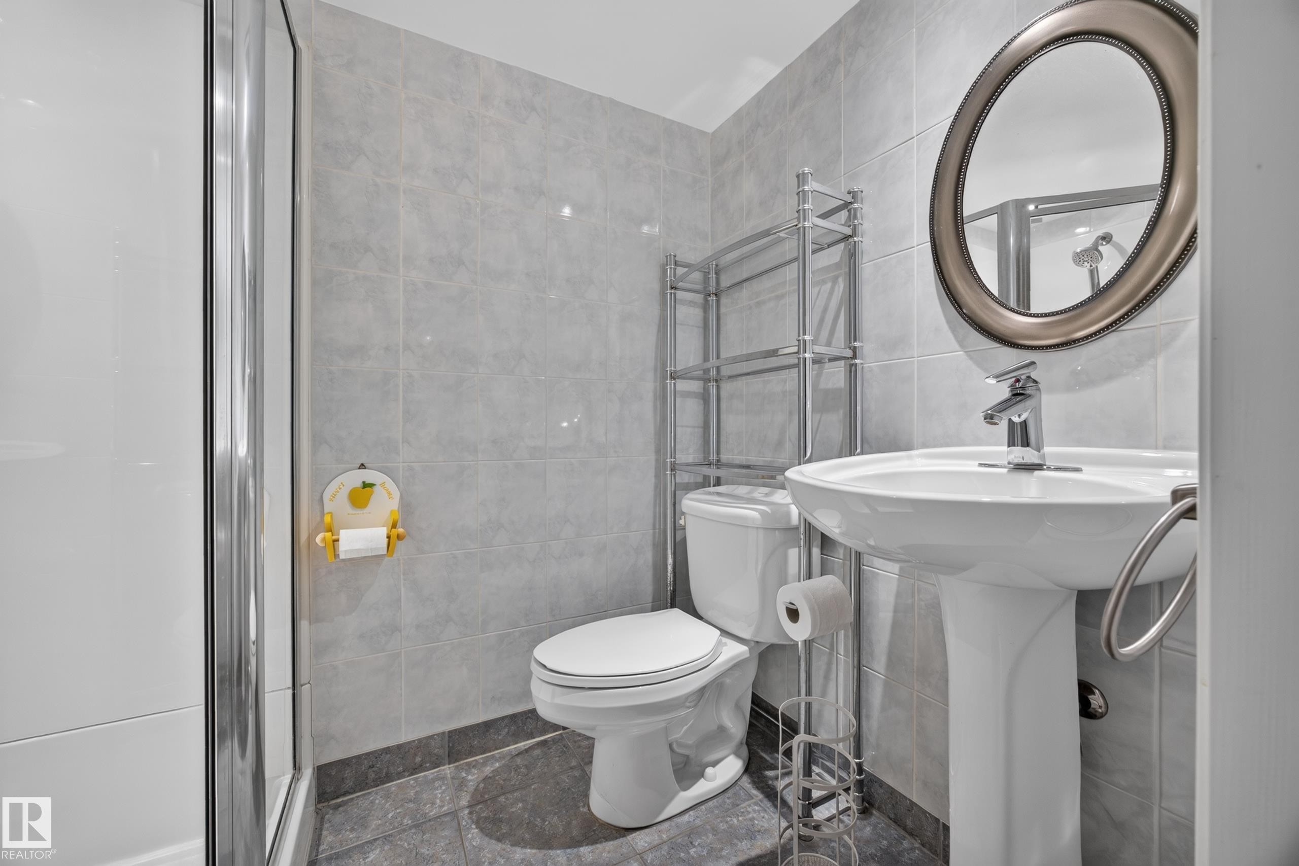 Pedestal sink with chrome faucet, oval mirror, and tiled shower enclosure - 9615 75 Avenue Nw, Edmonton, AB