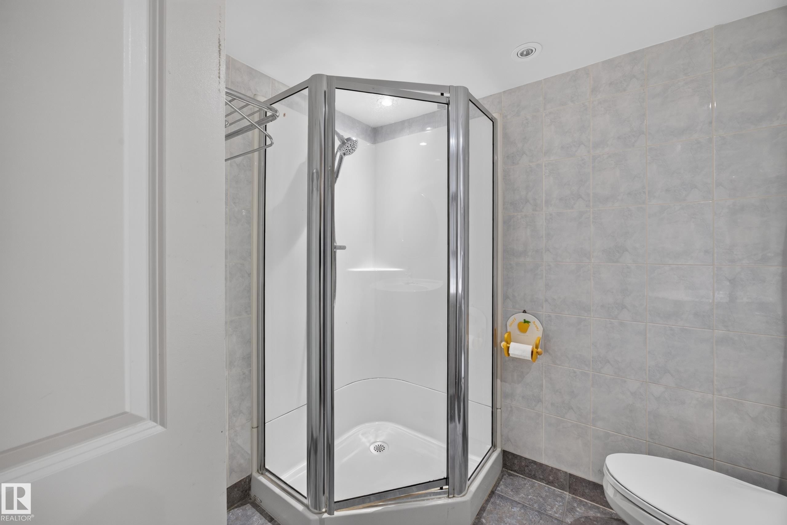 Glass-enclosed corner shower with a polished chrome frame, white shower base, and integrated shelving - 9615 75 Avenue Nw, Edmonton, AB
