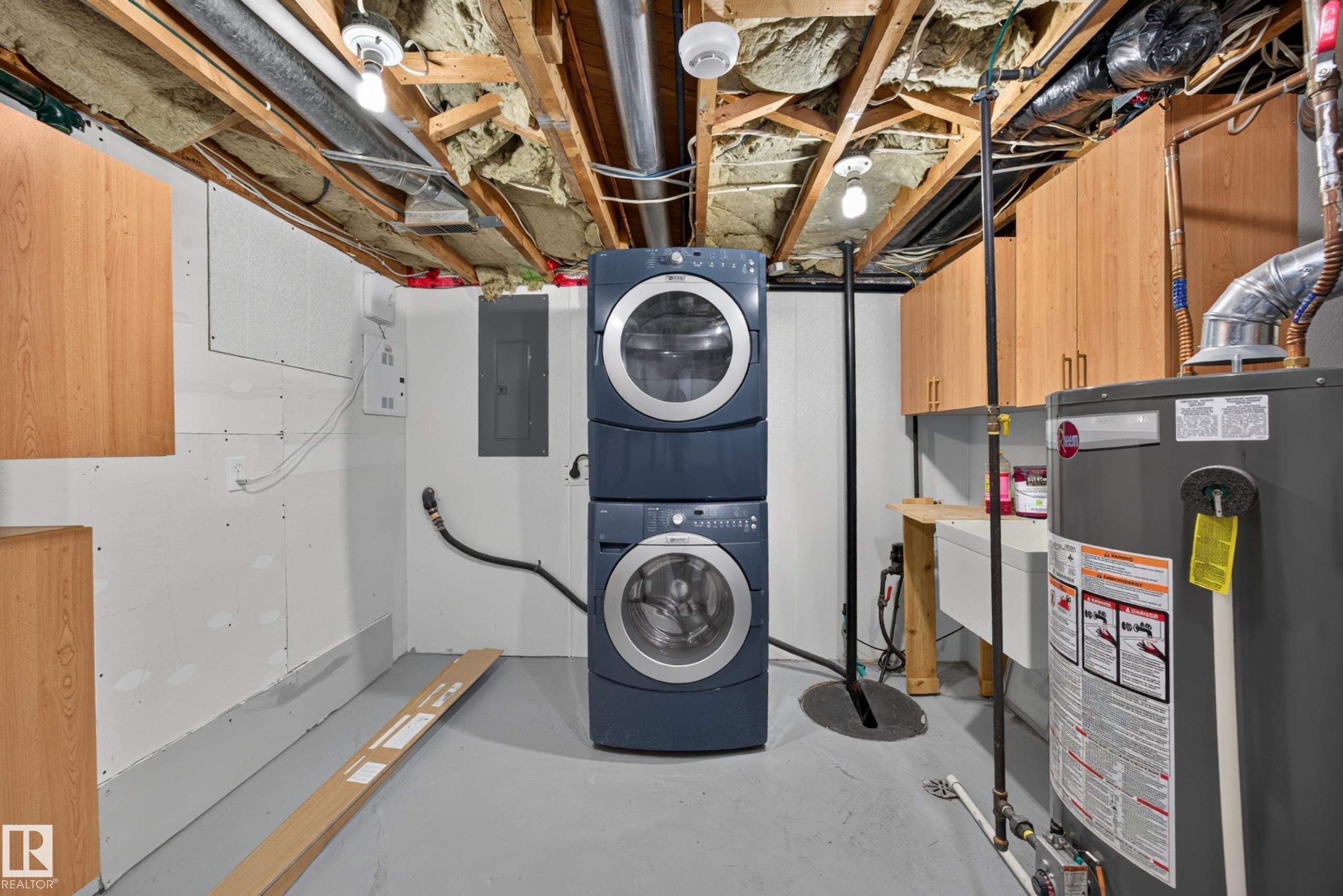 Laundry area featuring a stackable washer and dryer, wood-finish cabinetry, a utility sink, and a water heater - 9615 75 Avenue Nw, Edmonton, AB