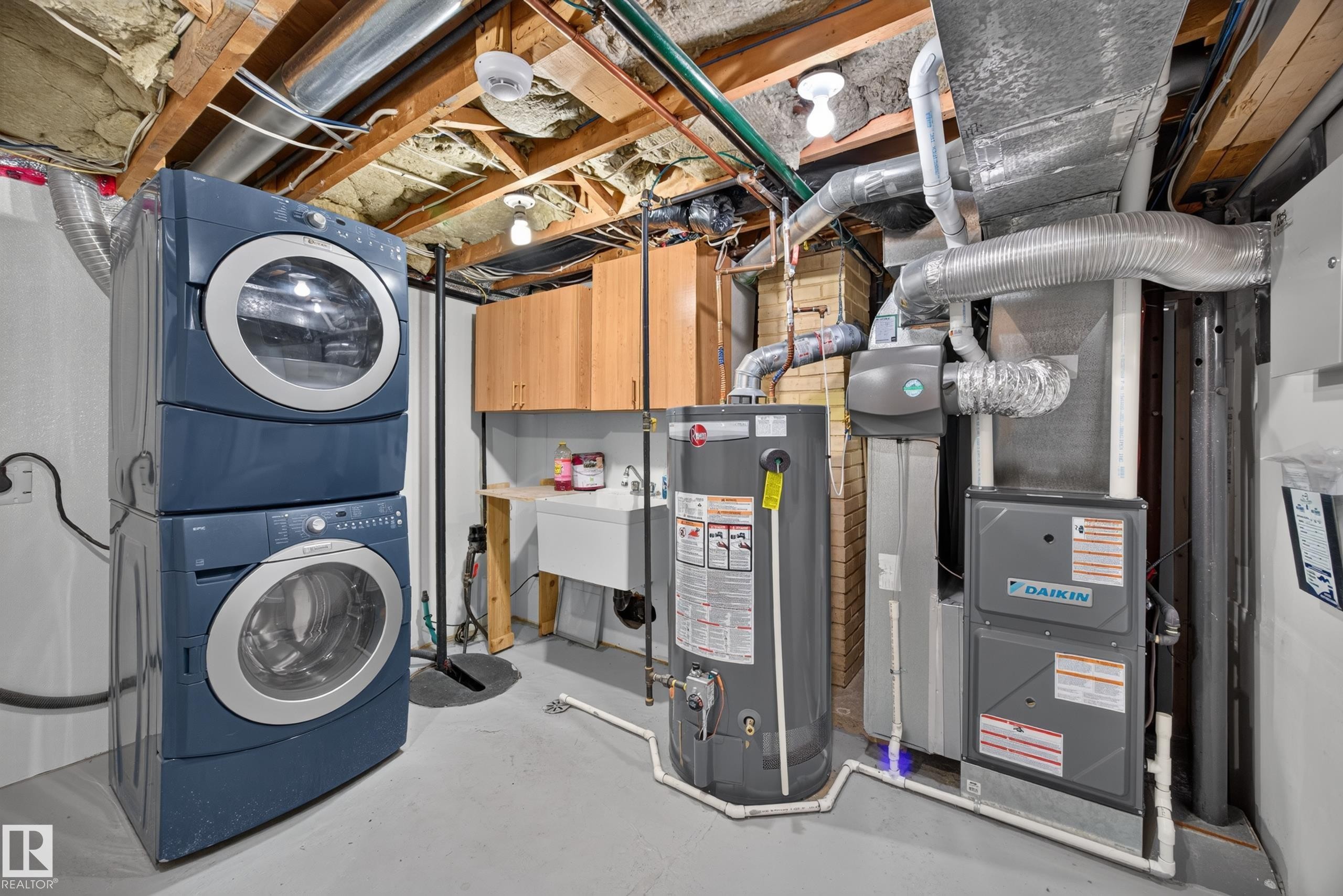Utility space featuring a stacked washer and dryer, laundry sink, and wood-finish cabinetry - 9615 75 Avenue Nw, Edmonton, AB