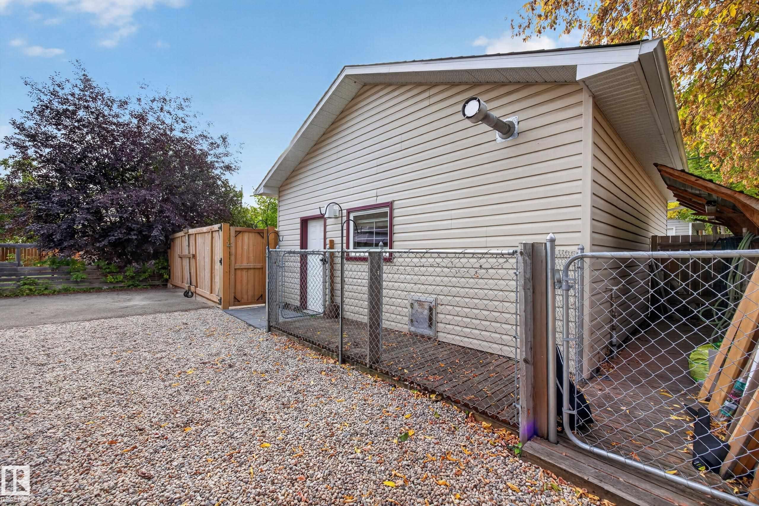 Exterior with light-colored siding, a gravel driveway, and a wooden privacy fence - 9615 75 Avenue Nw, Edmonton, AB