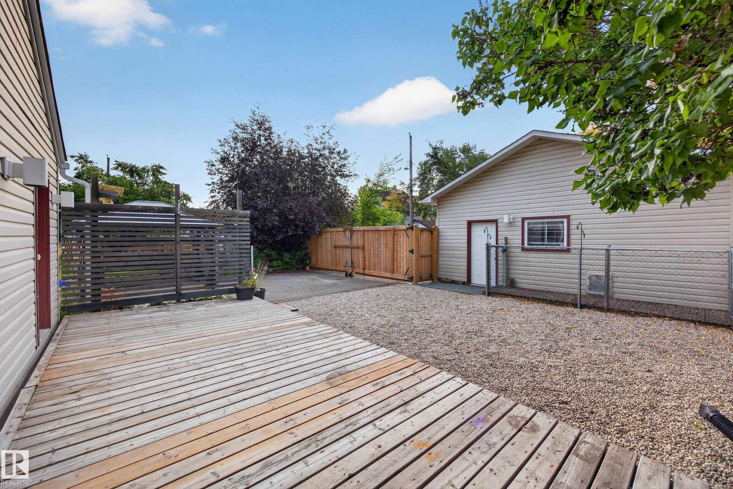Expansive wood deck with a privacy screen, gravel hardscaping, and a detached structure with siding - 9615 75 Avenue Nw, Edmonton, AB