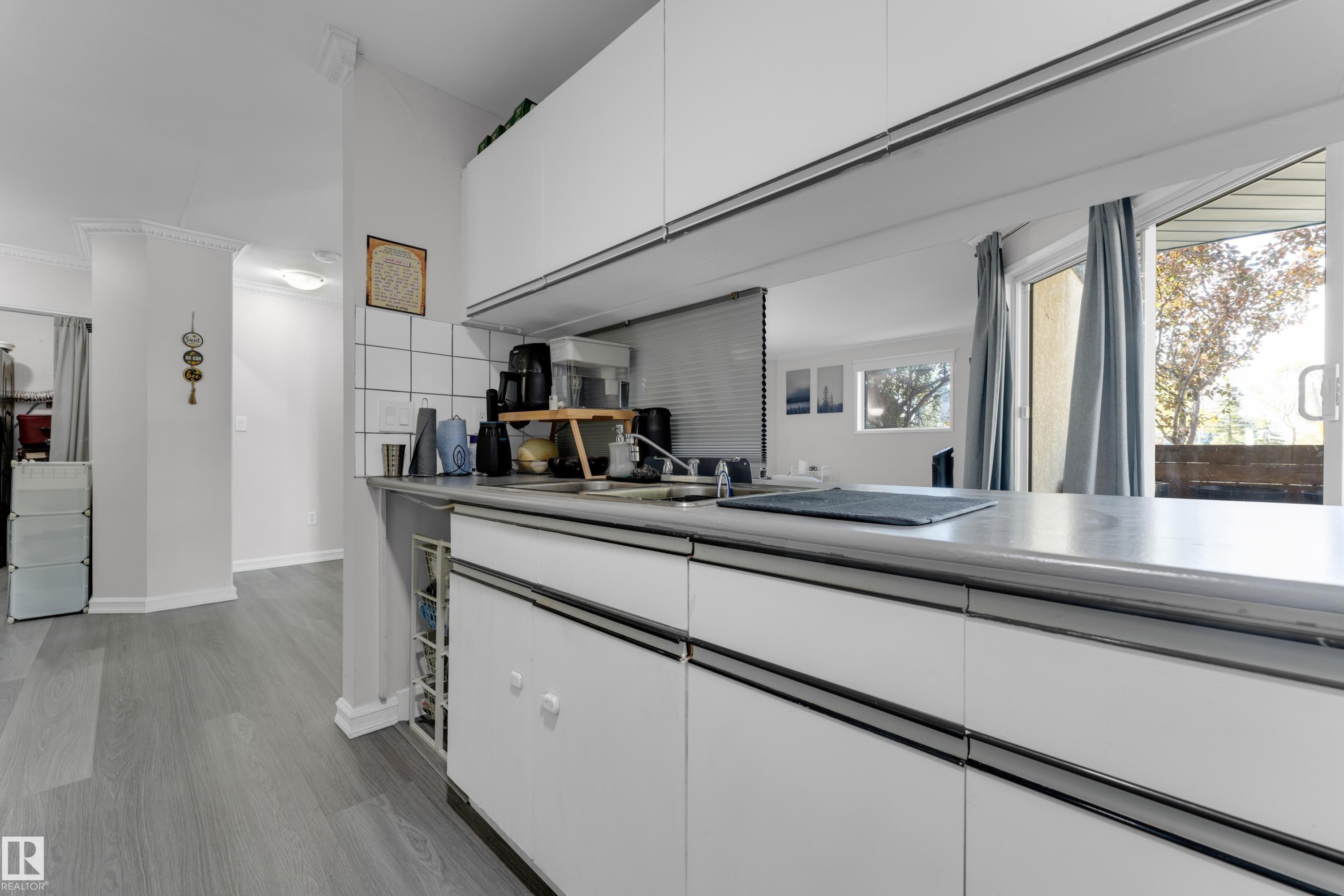 Modern kitchen featuring sleek white cabinetry with integrated hardware, stainless steel countertops, built-in appliances, and abundant natural light from expansive windows - #113 2508 50 St Nw, Edmonton, AB