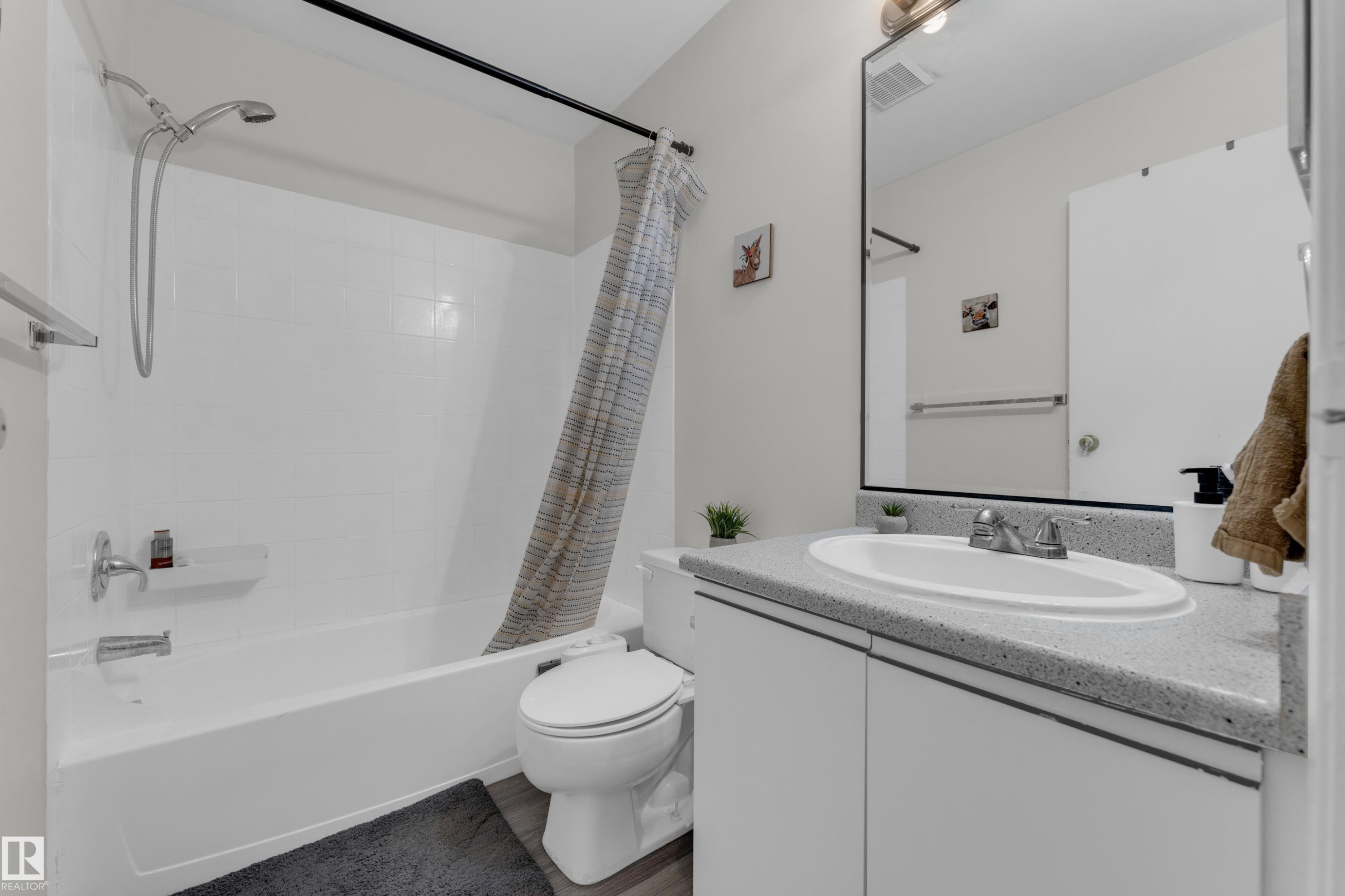 Bathroom with a white vanity featuring a built-in sink, speckled countertop, and wood-finish flooring - #113 2508 50 St Nw, Edmonton, AB