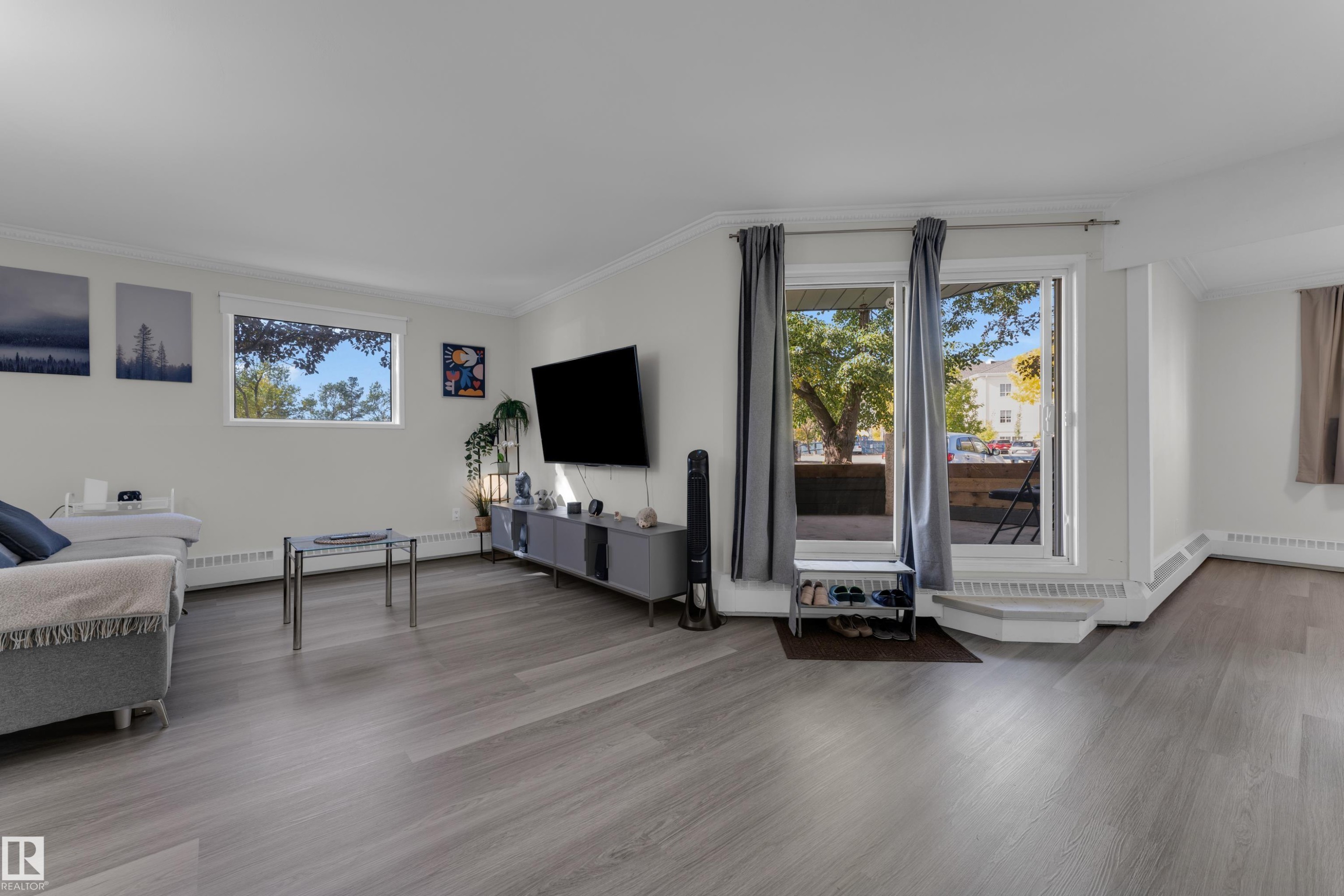 Spacious living area featuring wood-finish flooring, white walls, and bright windows - #113 2508 50 St Nw, Edmonton, AB