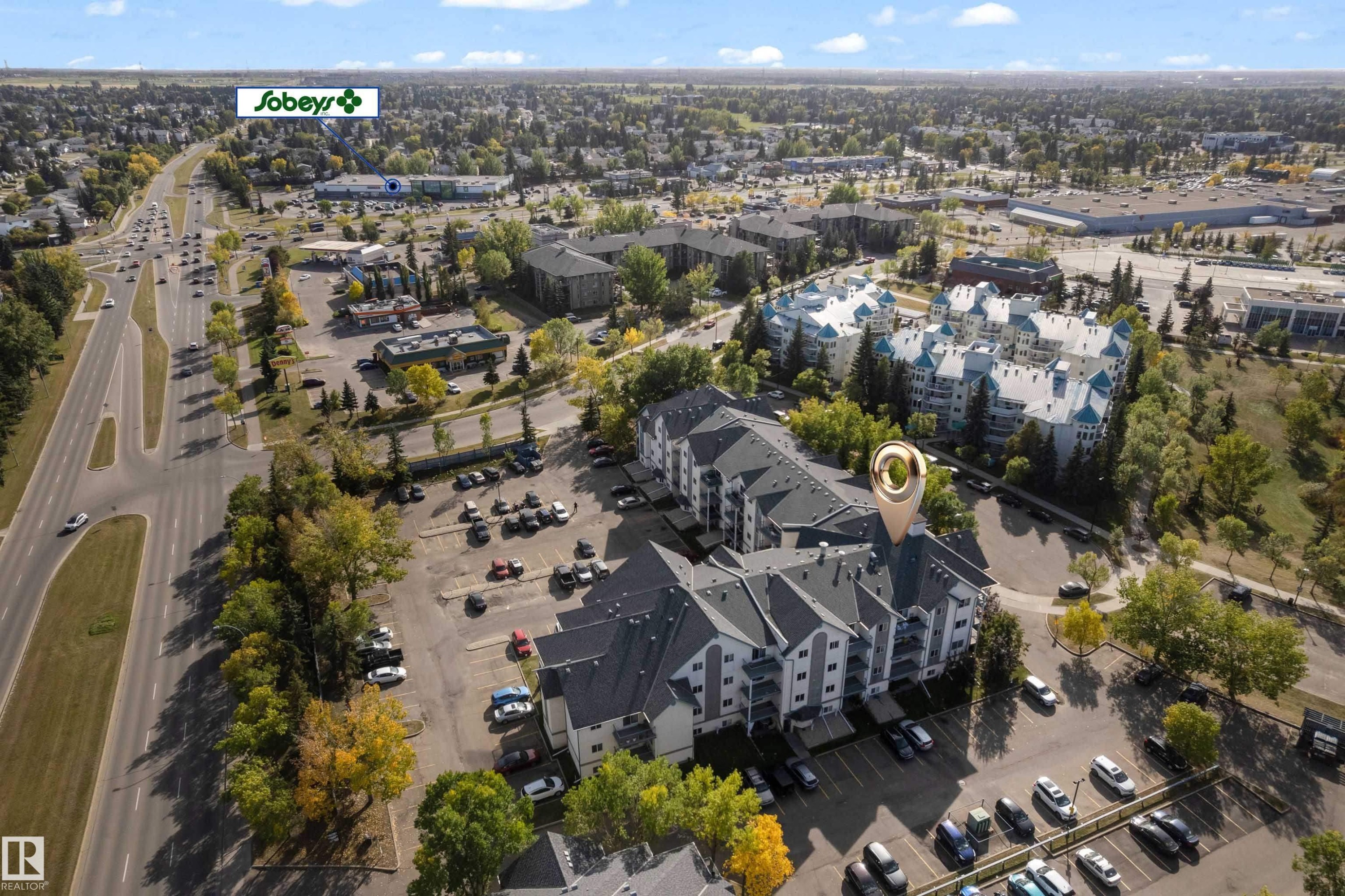 Multi-story residential buildings with pitched roofs, surrounded by mature trees and paved parking areas - #113 2508 50 St Nw, Edmonton, AB