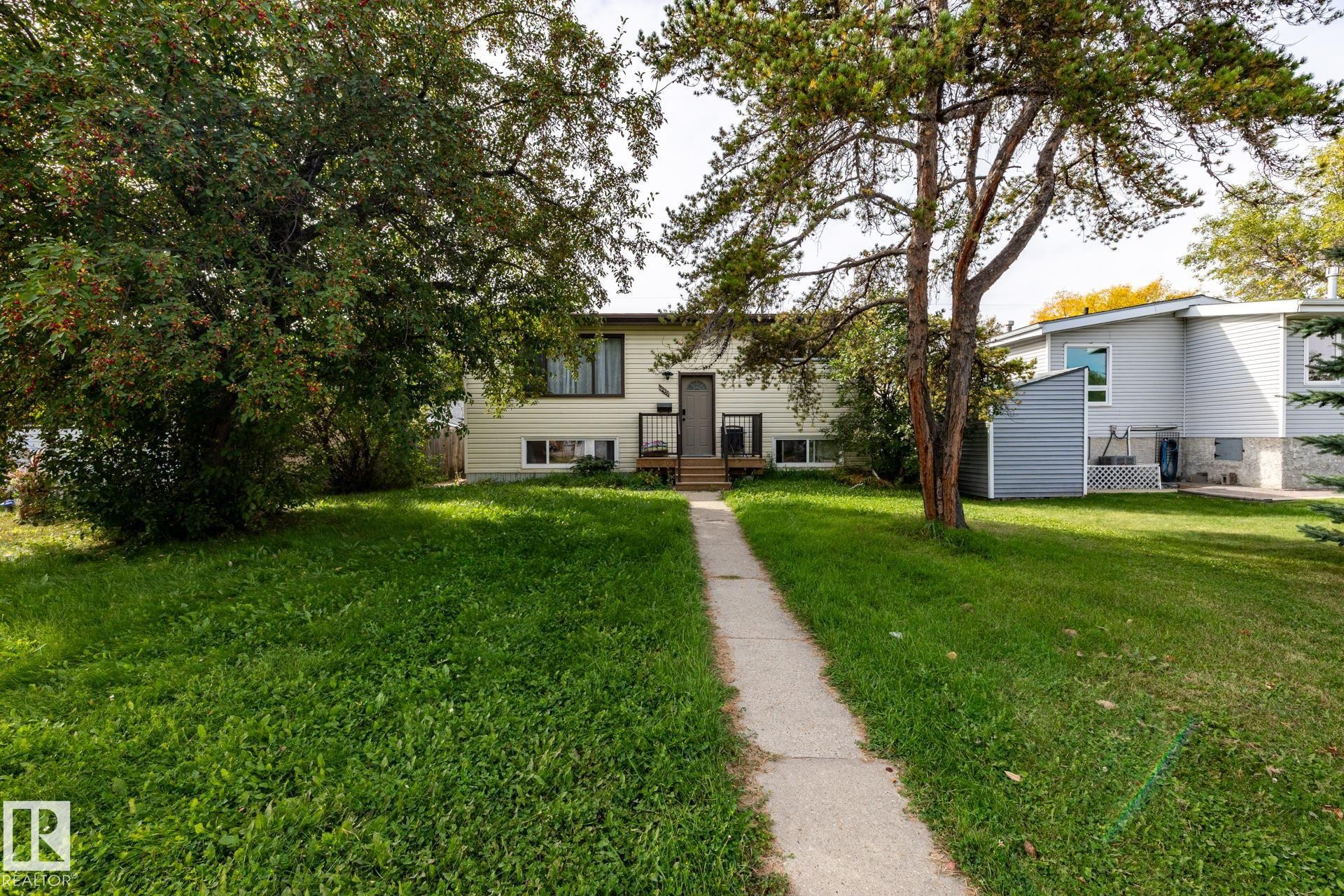 Front exterior with light-colored siding, dark trim windows, and a concrete walk-up leading to the entrance - 10972 157 Street Nw, Edmonton, AB