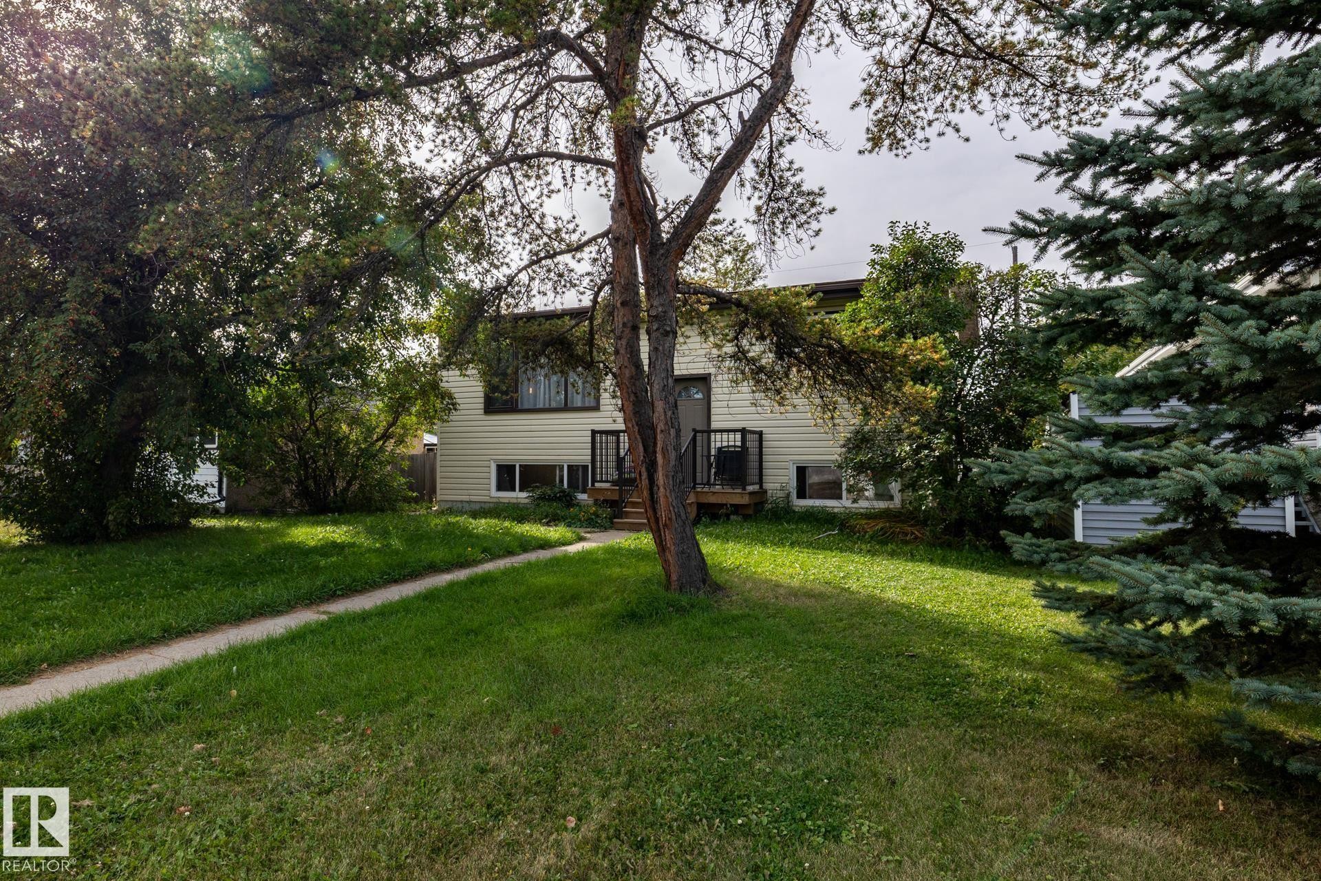 Light-colored siding exterior, dark trim windows, front entry deck with dark railings, mature trees, and a concrete walkway - 10972 157 Street Nw, Edmonton, AB