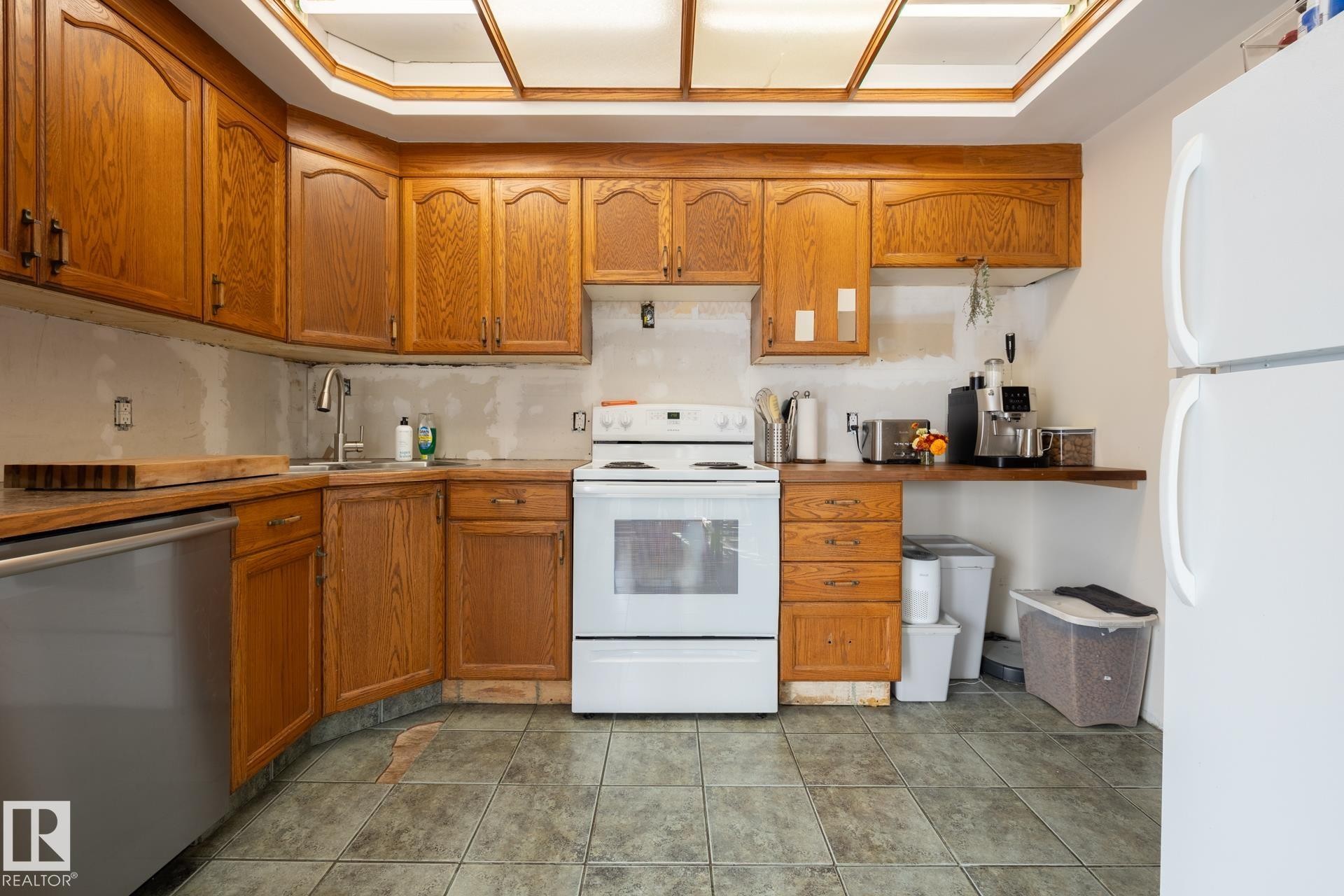 Kitchen featuring wood cabinetry, stainless steel dishwasher, white range, and tiled flooring - 10972 157 Street Nw, Edmonton, AB