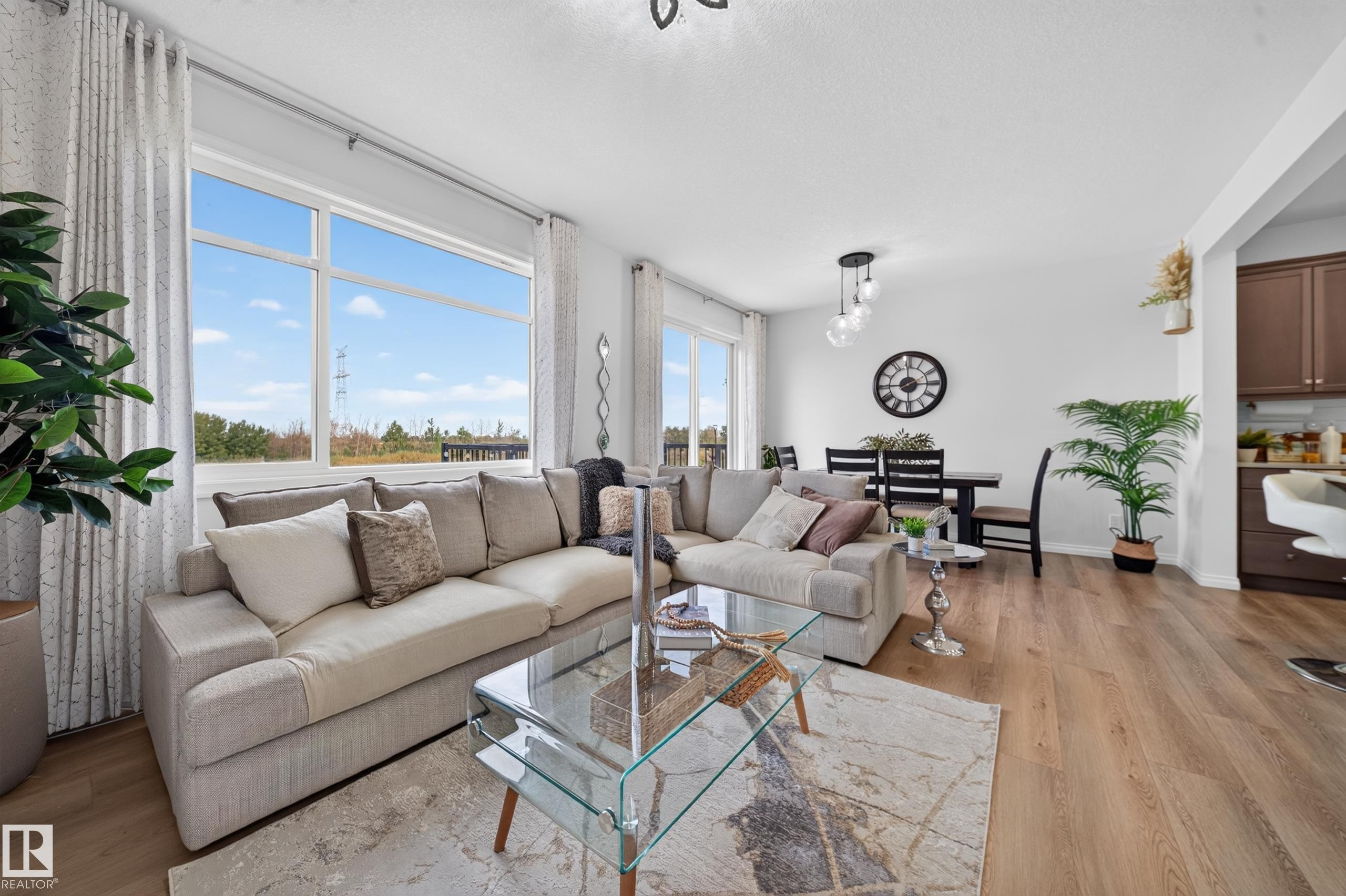 Open-concept living area featuring large windows, wood-finish flooring, and a dining space with a contemporary pendant light fixture - 4104 3 Avenue Sw, Edmonton, AB