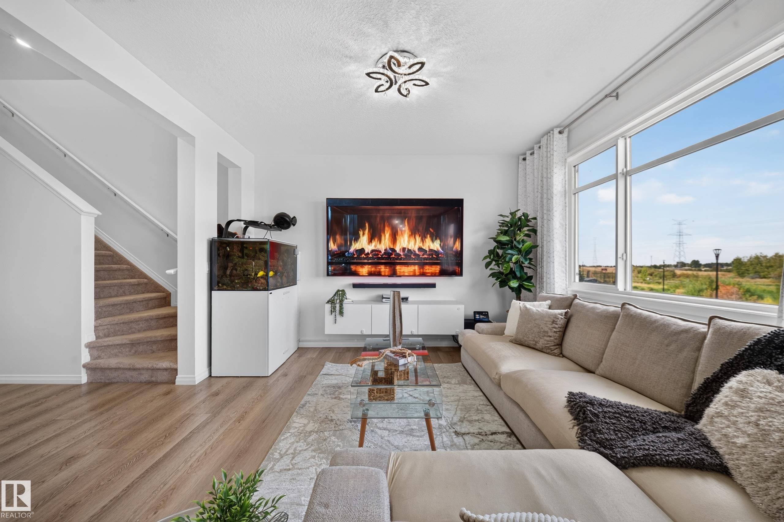 Bright living area featuring large windows, wood-finish flooring, a built-in media console, and a contemporary ceiling fixture - 4104 3 Avenue Sw, Edmonton, AB