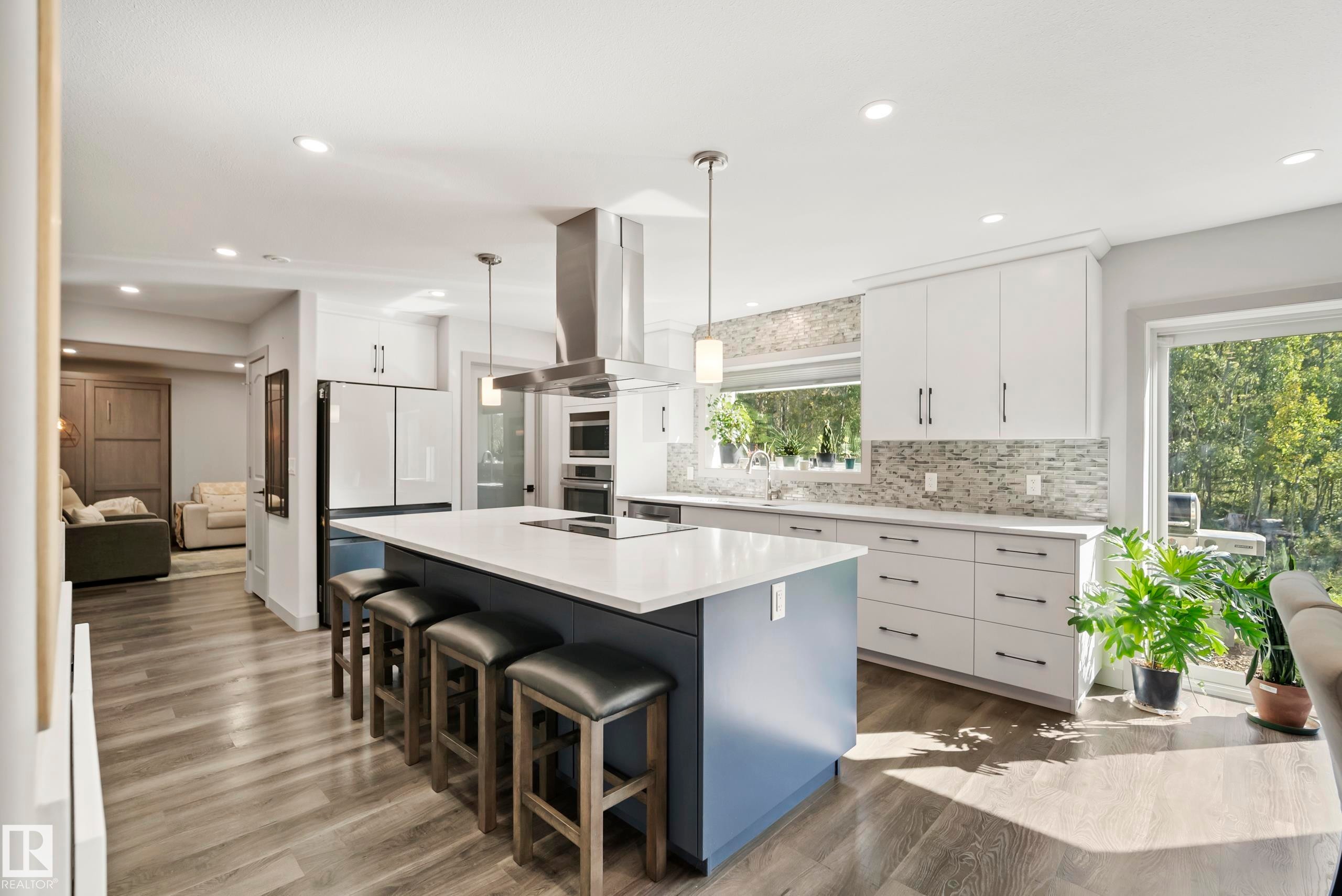 Kitchen featuring a large island with seating, pendant lighting, stainless steel range hood, built-in appliances, and wood-finish flooring - 49279 Rge Rd 240, Rural Leduc County, AB