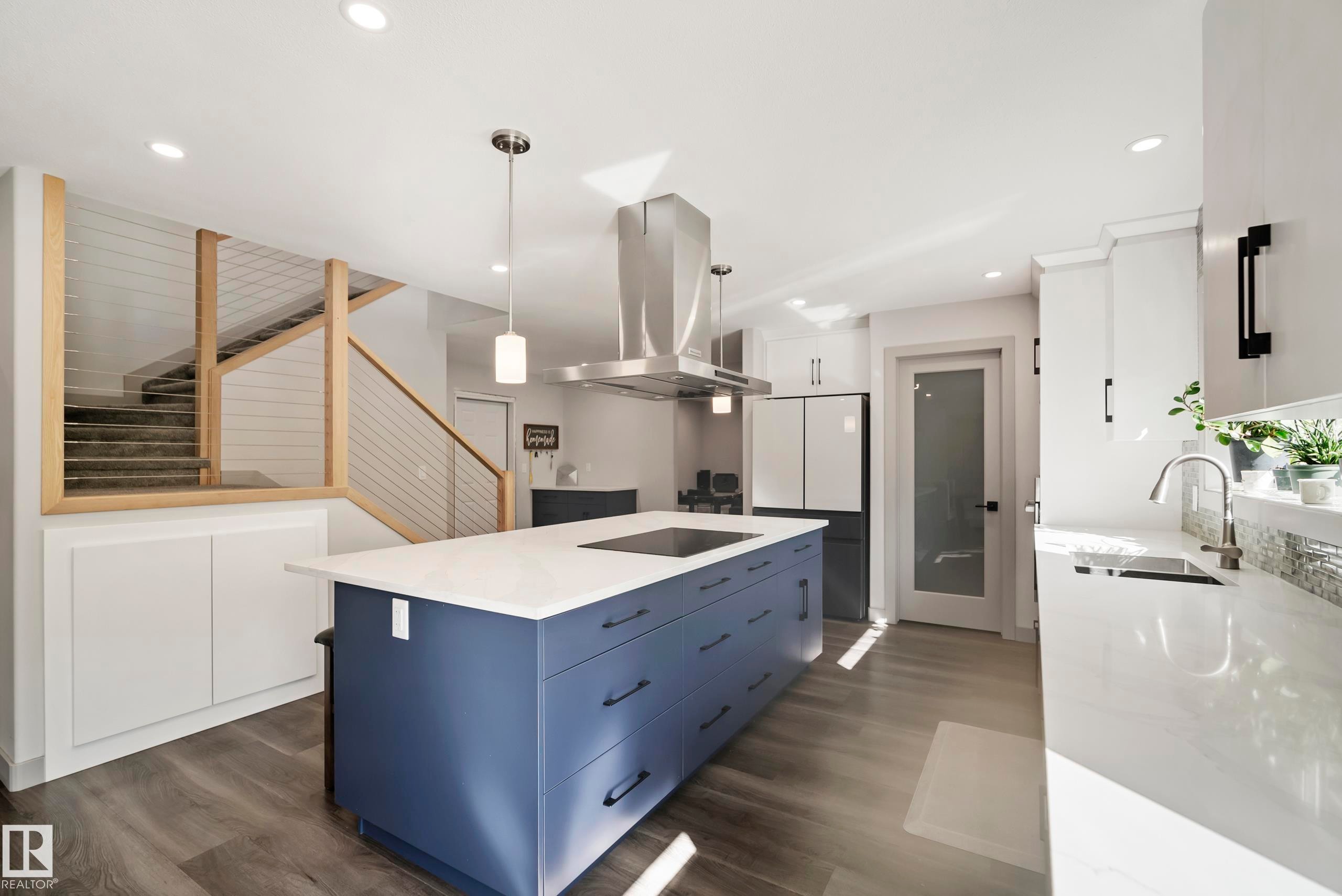 Kitchen featuring a blue island with a built-in cooktop, stainless steel range hood, white countertops, and wood-finish flooring - 49279 Rge Rd 240, Rural Leduc County, AB