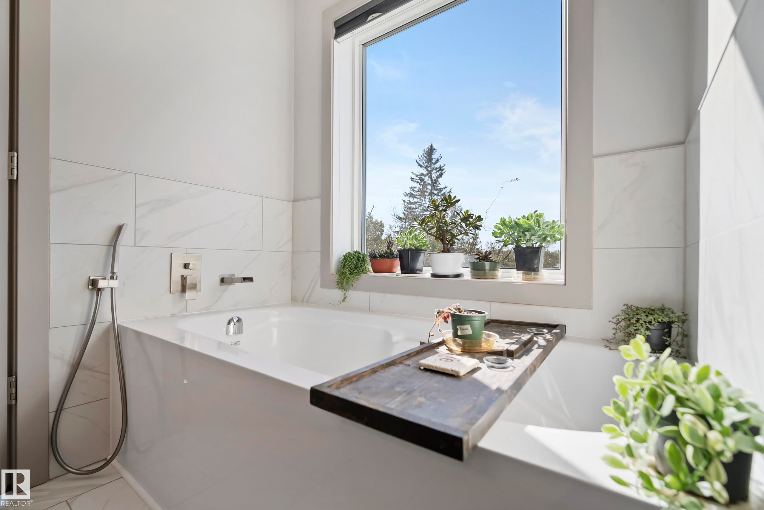 Built-in soaking tub with a wall-mounted faucet, handheld shower fixture, and a large window - 49279 Rge Rd 240, Rural Leduc County, AB