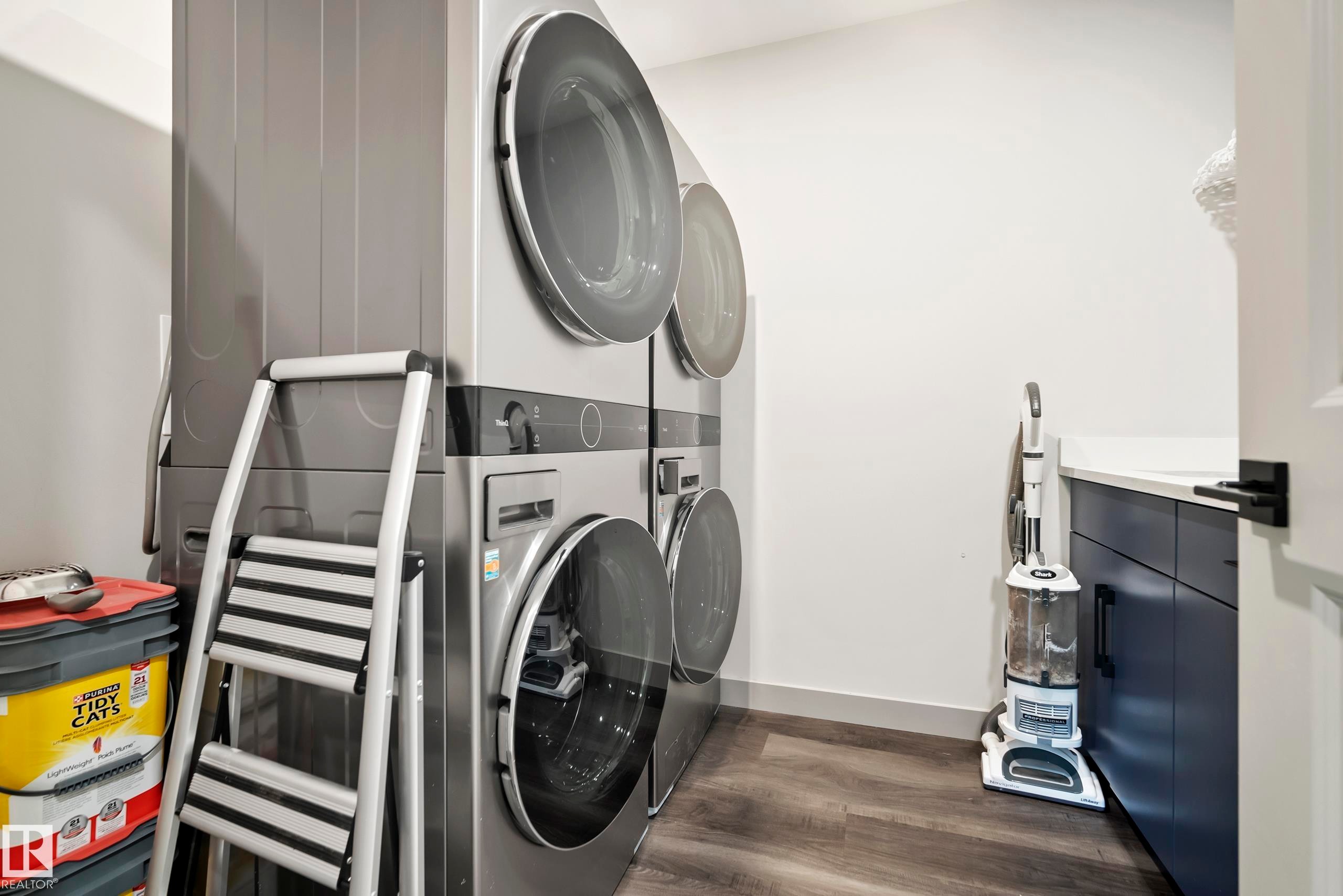 Laundry area featuring wood-finish flooring, white walls, and dark cabinetry with a light-colored countertop - 49279 Rge Rd 240, Rural Leduc County, AB