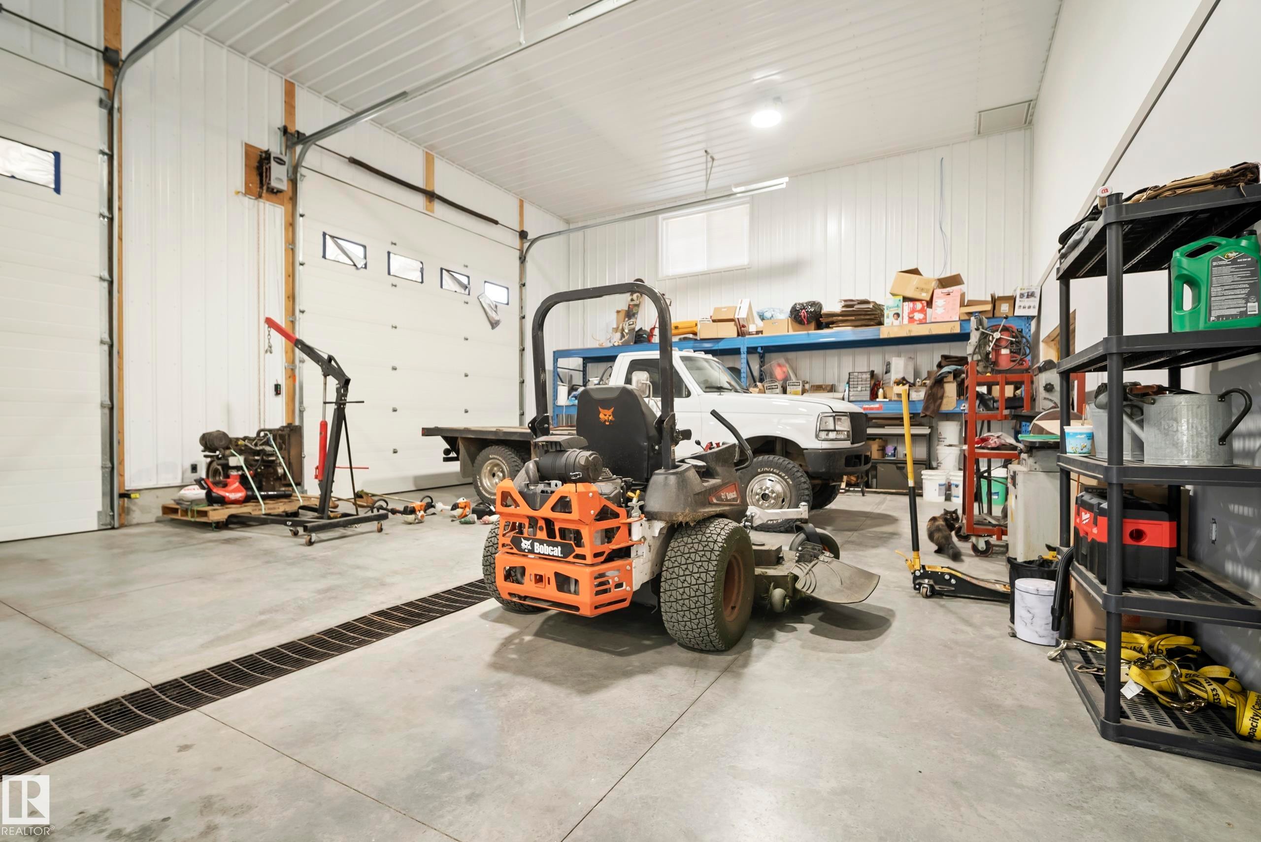 Spacious garage featuring high ceilings, two large overhead doors with windows, a concrete floor with an integrated trench drain, and functional overhead lighting - 49279 Rge Rd 240, Rural Leduc County, AB