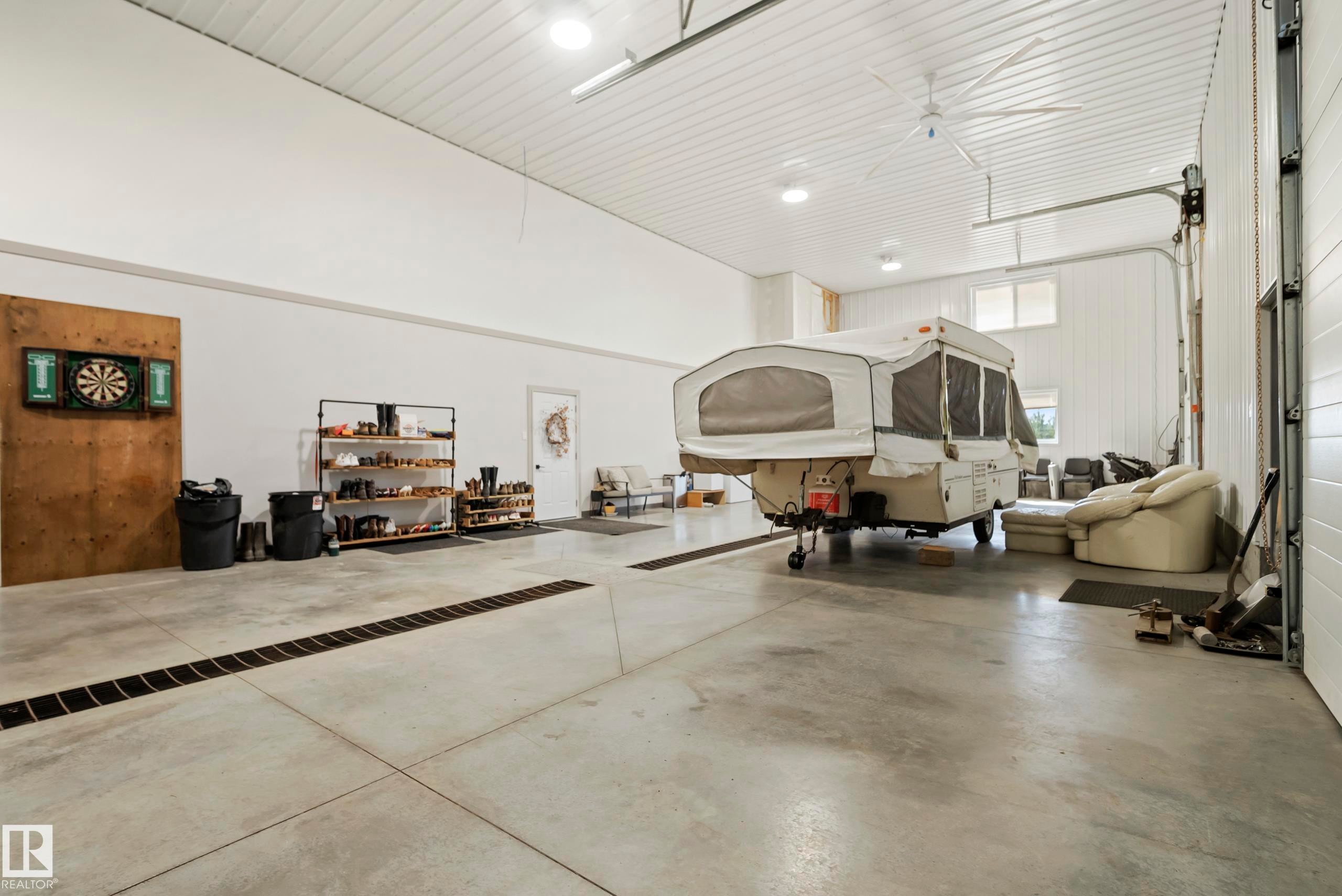 Spacious concrete floor with integrated drainage, white panel walls, and a large ceiling fan - 49279 Rge Rd 240, Rural Leduc County, AB