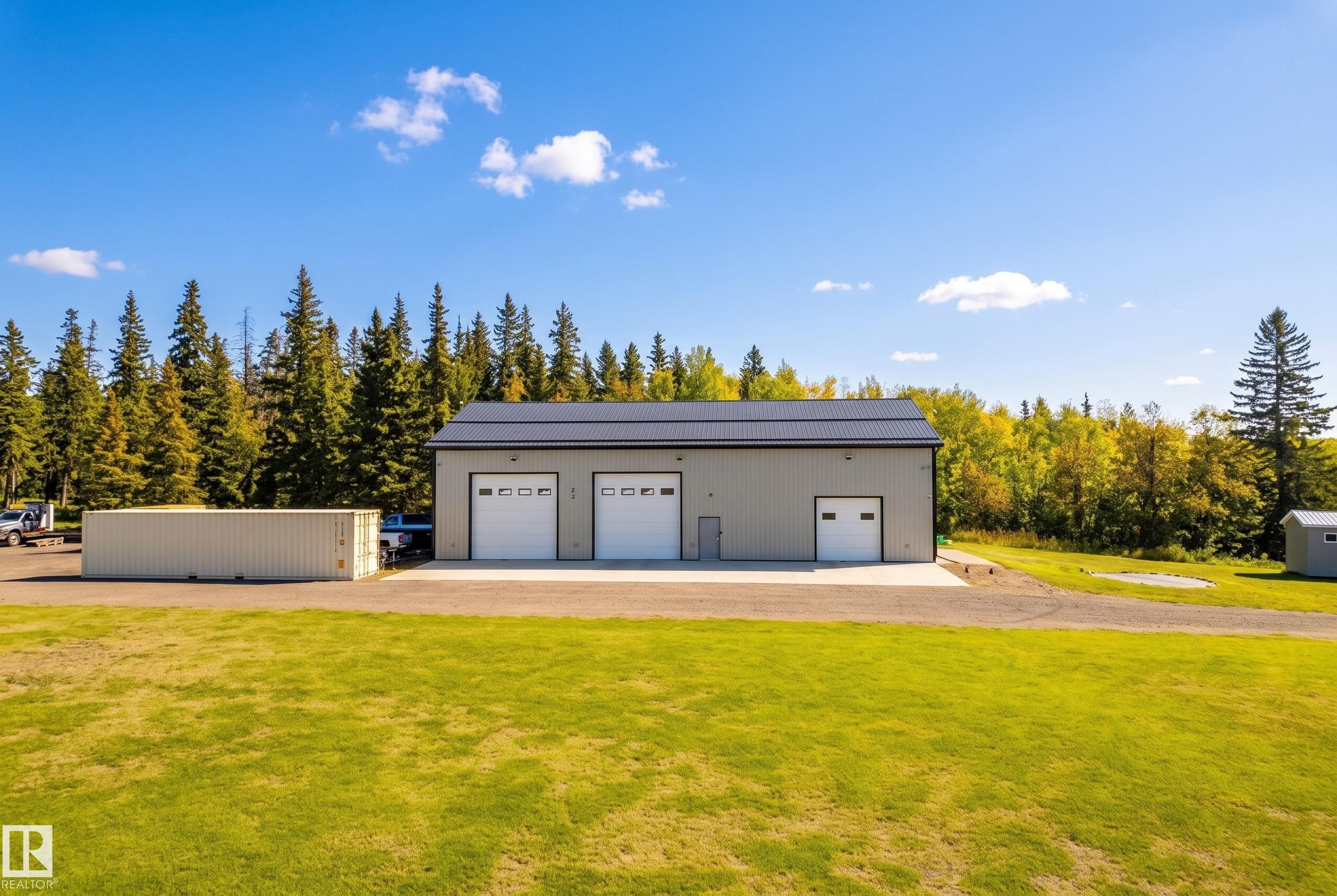 Two-story metal building featuring multiple roll-up doors, a flat roof, and a gravel driveway and home - 49279 Rge Rd 240, Rural Leduc County, AB