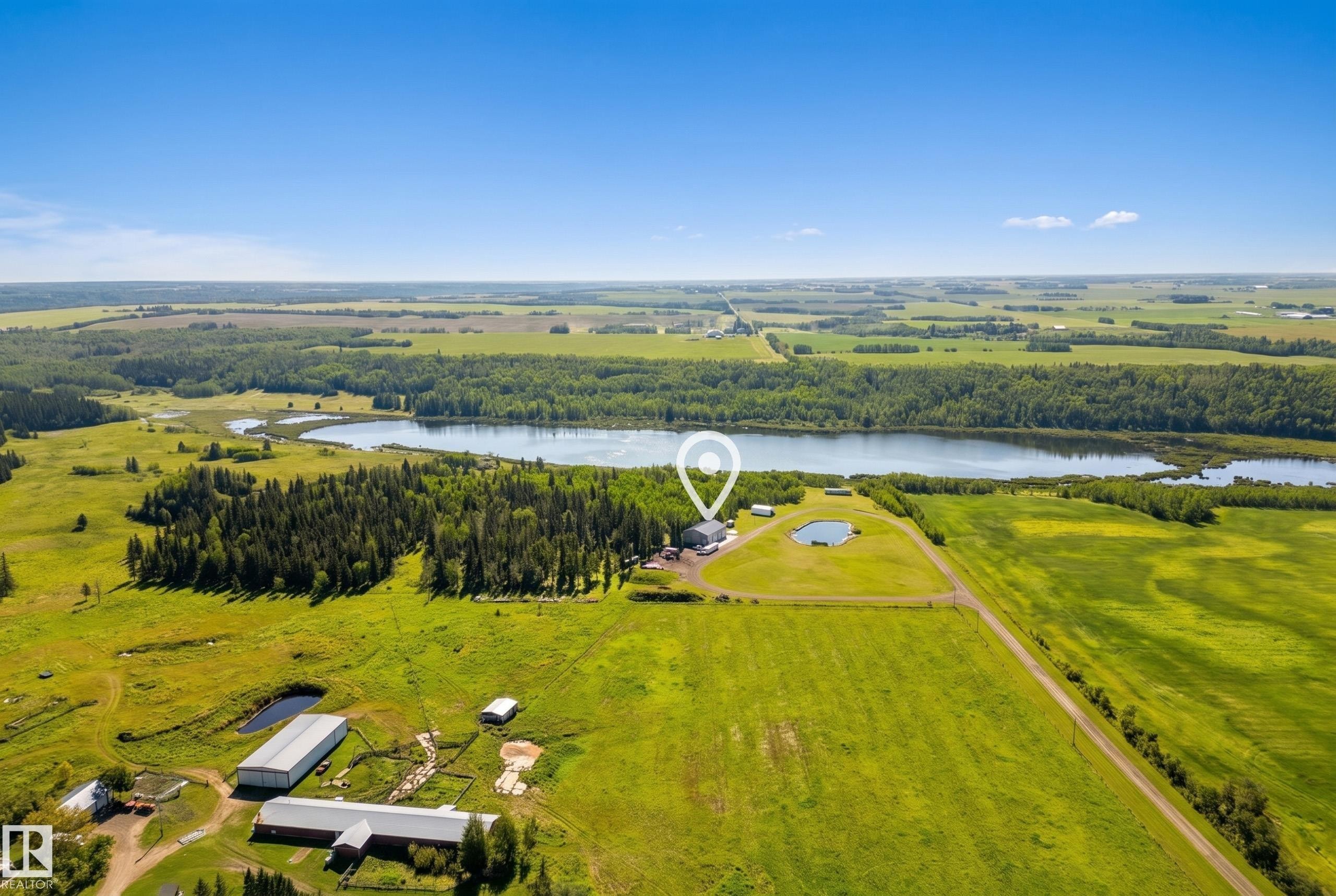 Expansive property featuring a large body of water, dense tree lines, and multiple agricultural structures - 49279 Rge Rd 240, Rural Leduc County, AB