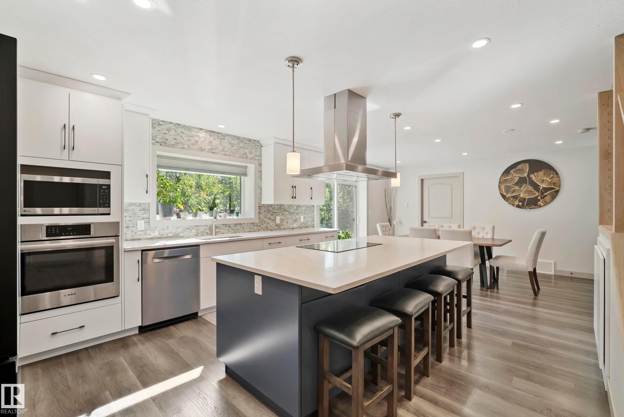 Kitchen featuring a large central island with seating, stainless steel appliances, white cabinetry, wood-finish flooring, and recessed lighting - 49279 Rge Rd 240, Rural Leduc County, AB
