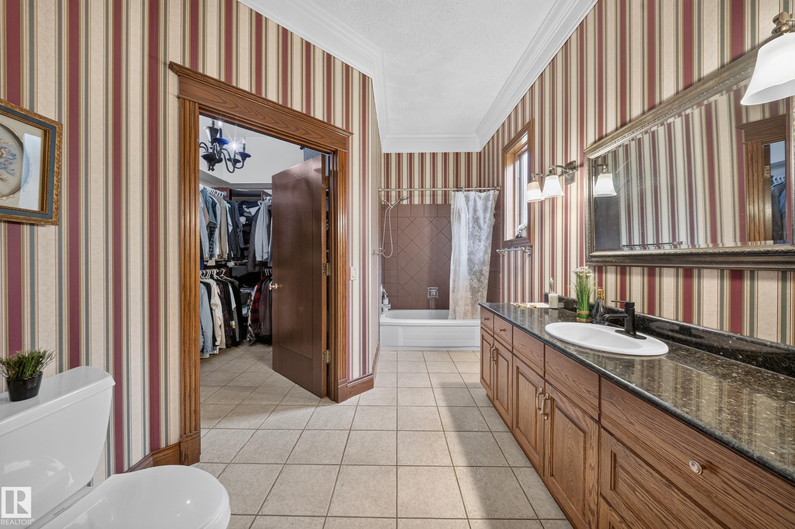 Ceramic tile flooring, built-in bathtub with tiled surround, wood-finish vanity with countertop, and an attached walk-in closet - 719 65 Ave Nw, Edmonton, AB