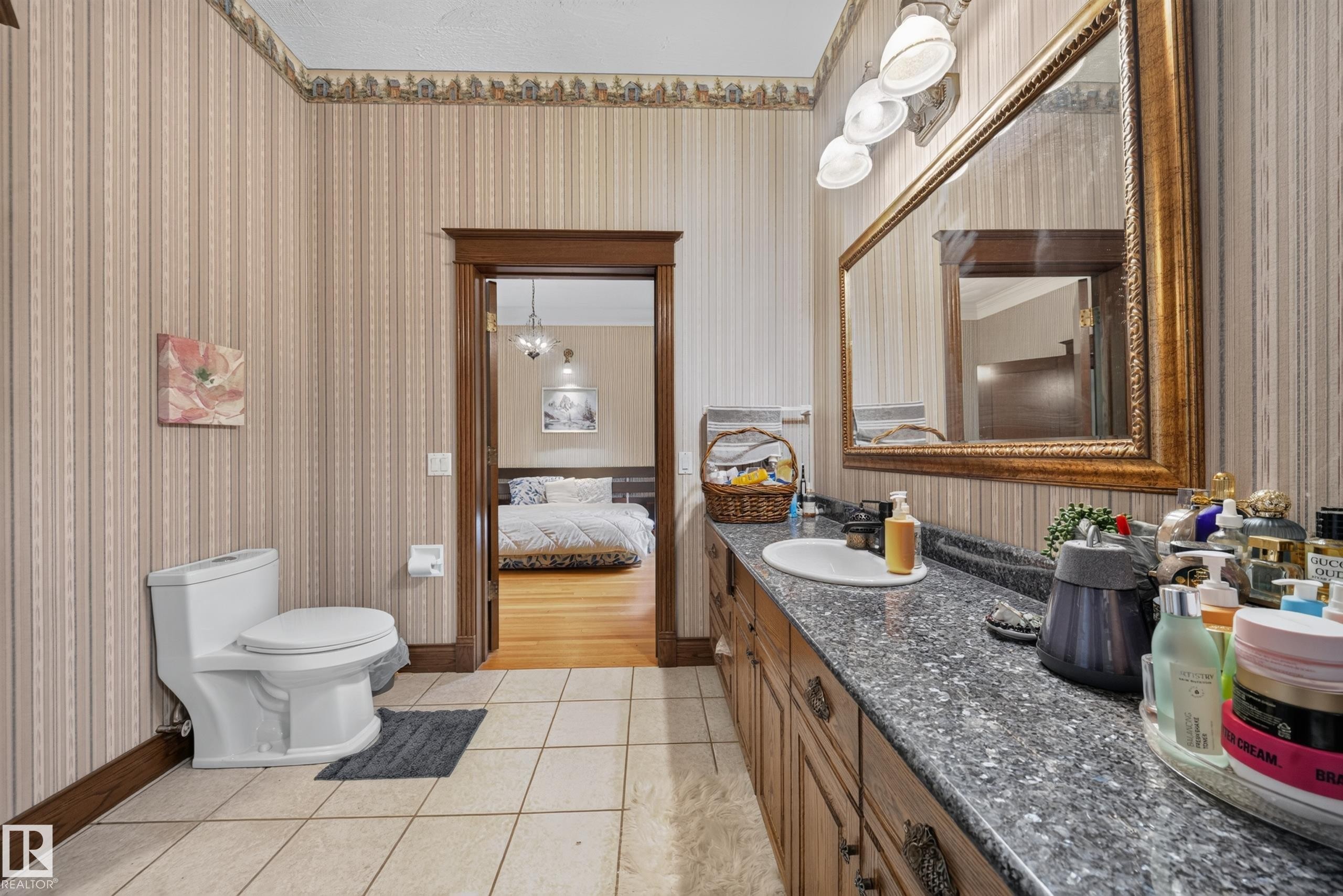 Bathroom featuring a white toilet, tiled flooring, wood-finish vanity with ample storage, and a large framed mirror - 719 65 Ave Nw, Edmonton, AB