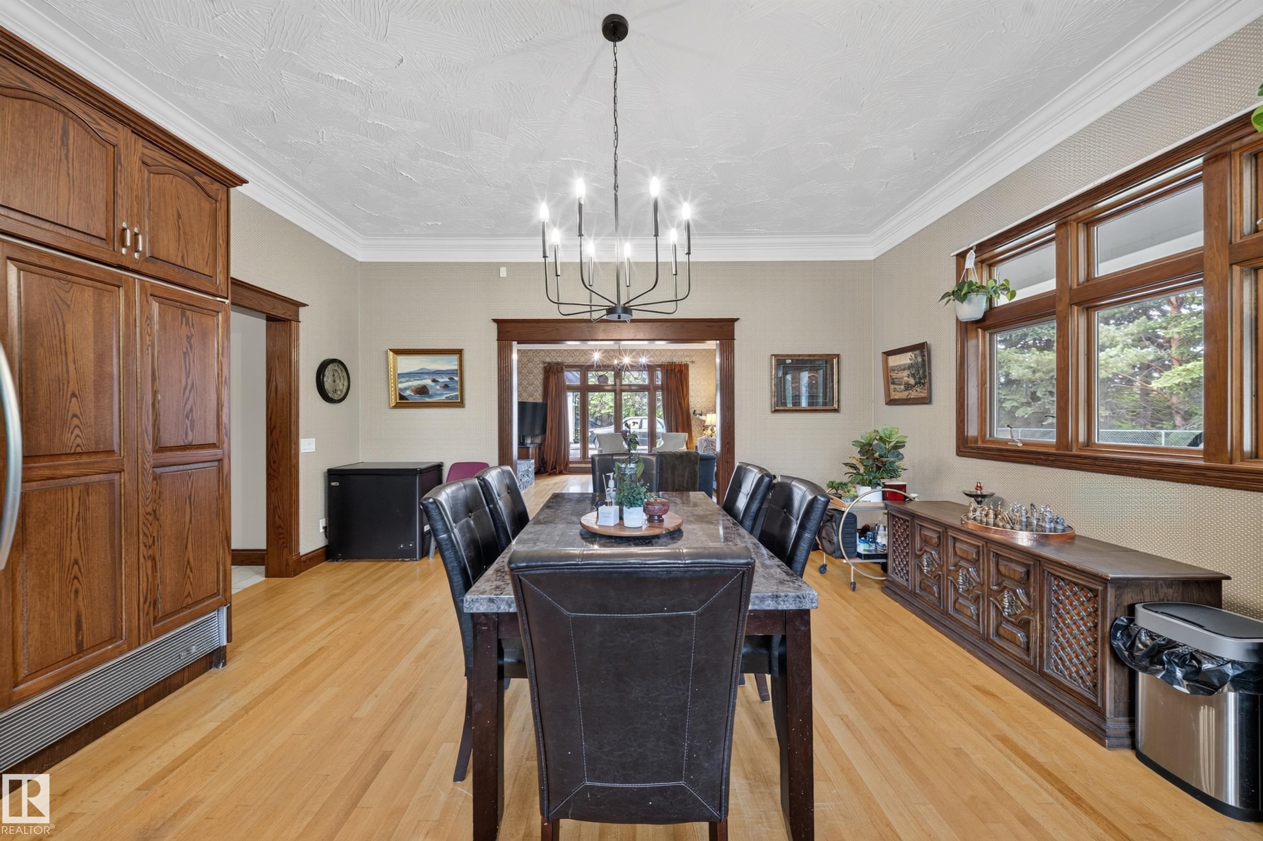 Wood-finish flooring with crown molding, a built-in wood-finish refrigerator, and a multi-light chandelier - 719 65 Ave Nw, Edmonton, AB