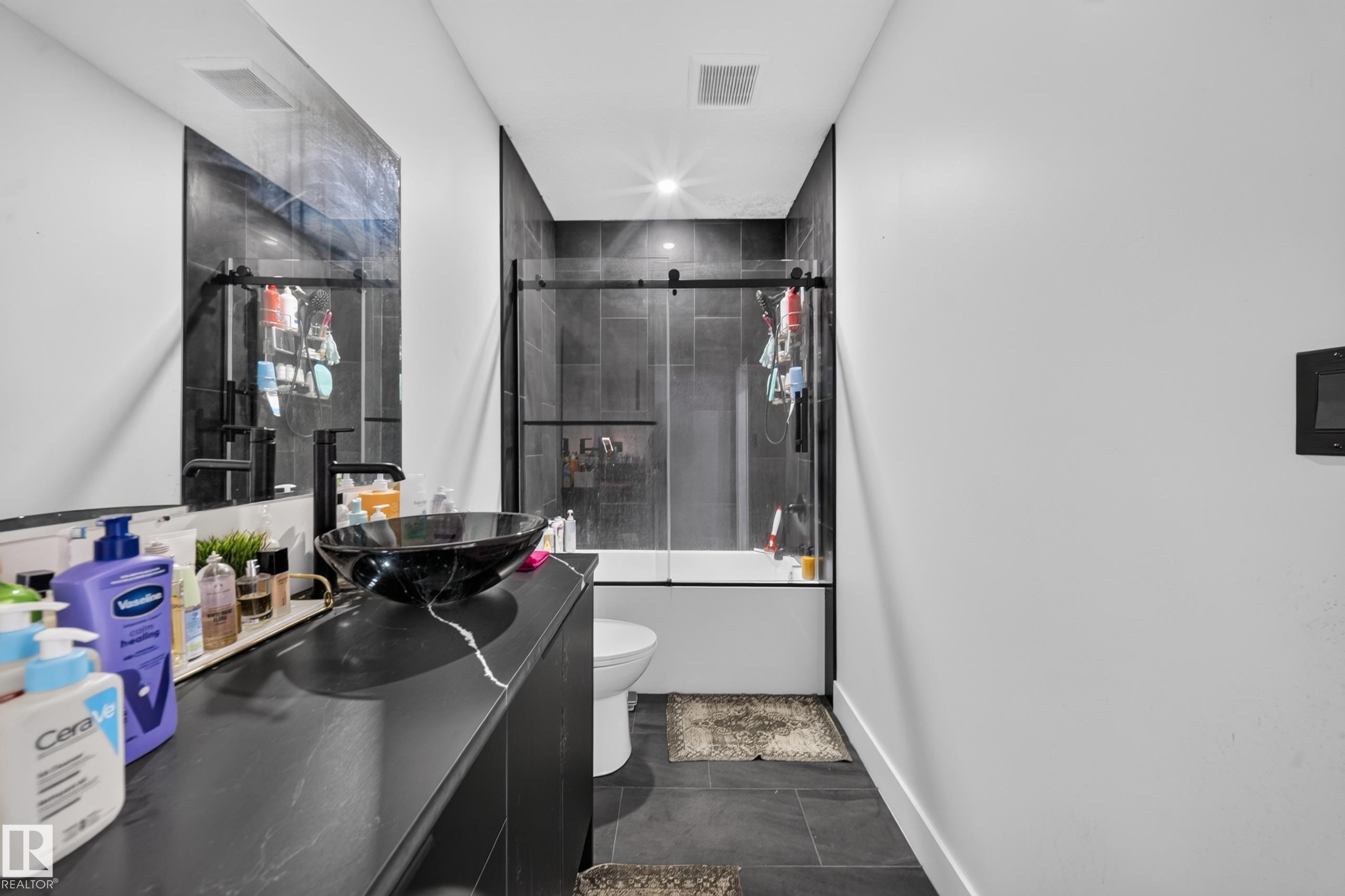 Vessel sink on a dark vanity, large wall mirror, and a tiled shower with a clear glass enclosure - 719 65 Ave Nw, Edmonton, AB