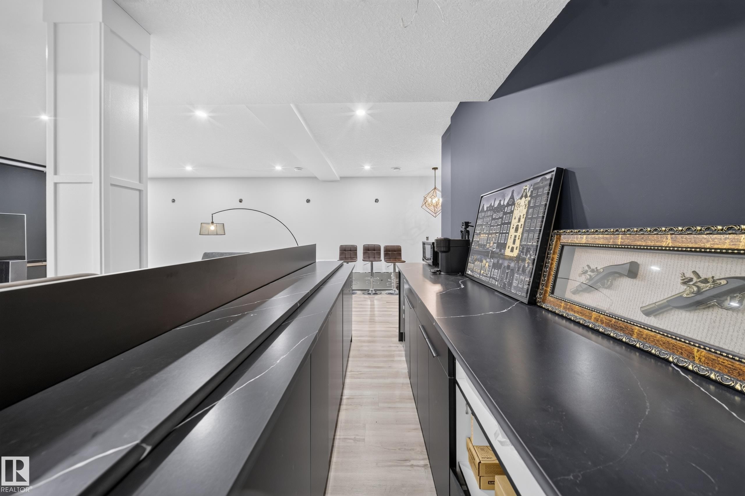 Dark cabinetry with integrated handles and a light-veined countertop, recessed ceiling lighting, light wood-finish flooring, and a dark accent wall - 719 65 Ave Nw, Edmonton, AB