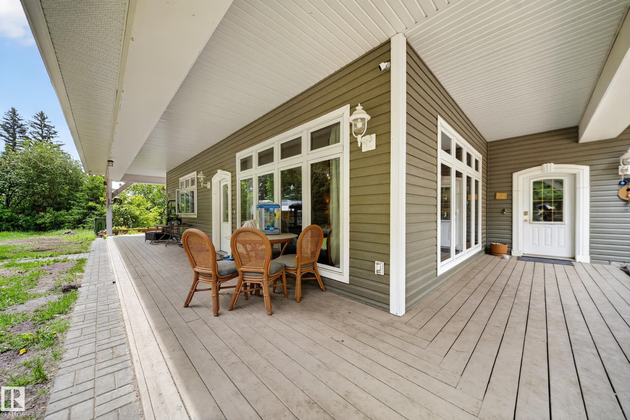 Expansive covered porch featuring a wood-finish floor, white trim, multiple windows, and a decorative entry door - 719 65 Ave Nw, Edmonton, AB
