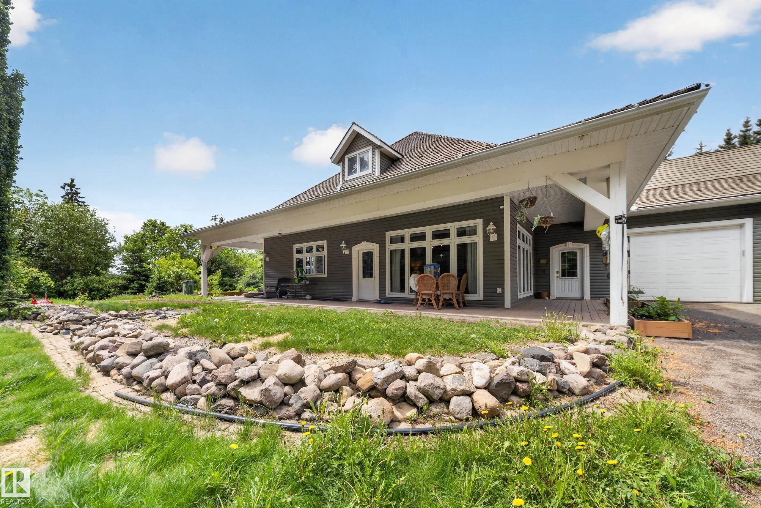 Gray siding exterior with white trim, covered patio, multiple glass panel doors, attached garage, and a gable dormer - 719 65 Ave Nw, Edmonton, AB
