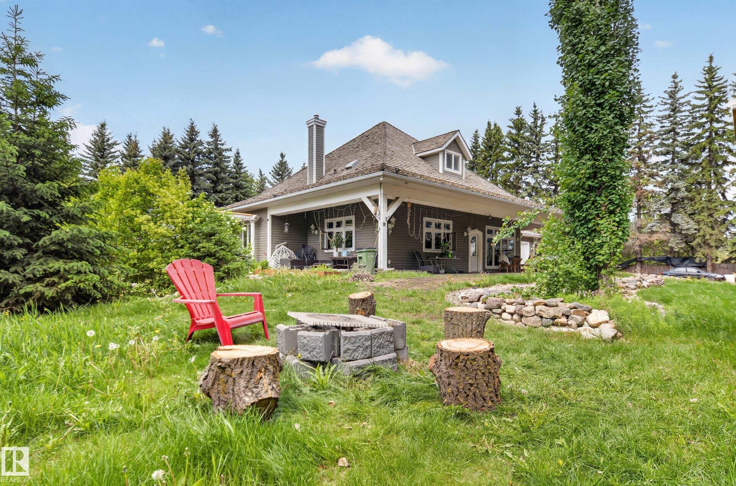 Expansive grassy area with a stone retaining wall, mature trees, and a fire pit - 719 65 Ave Nw, Edmonton, AB