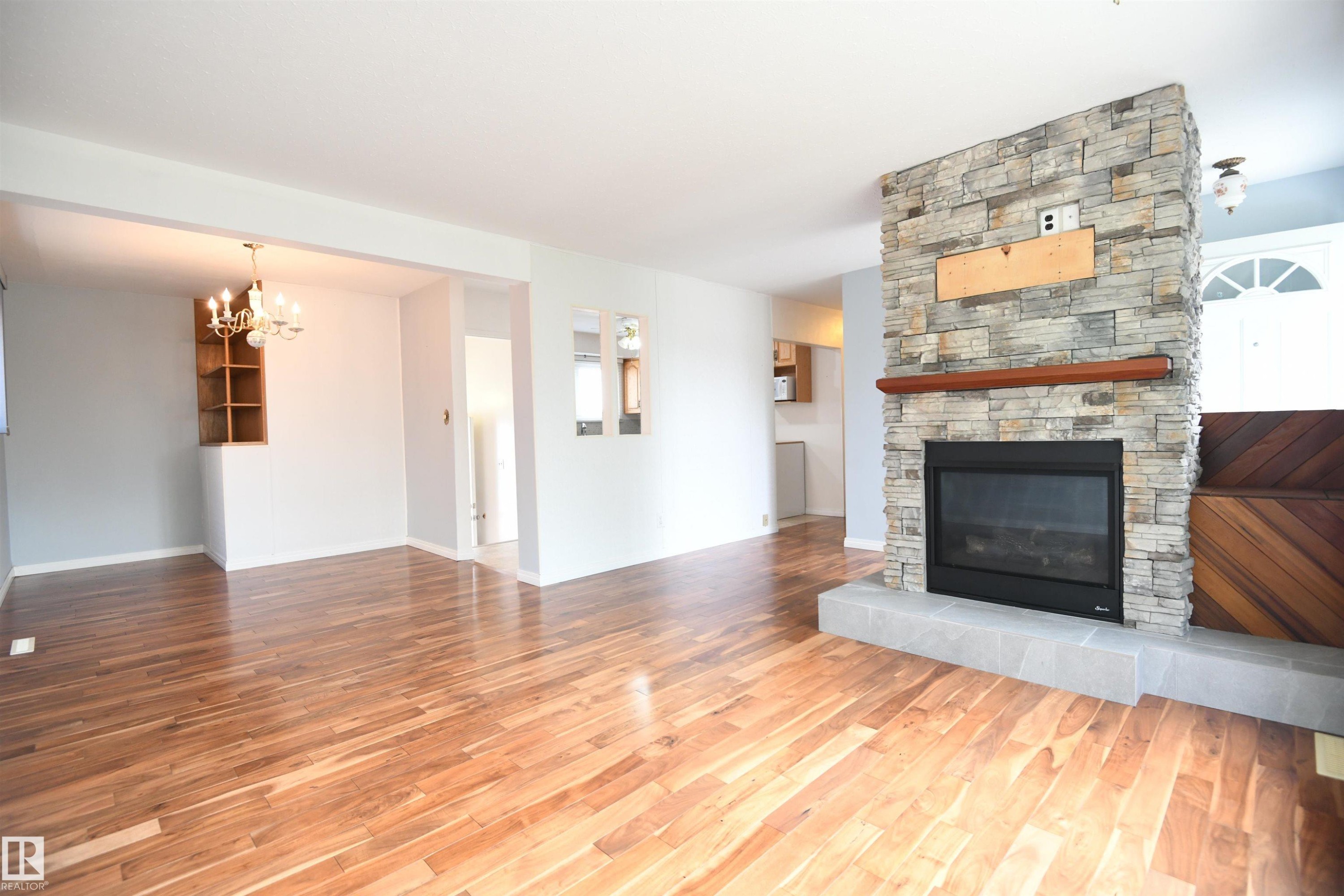Warm toned hardwood flooring flows through the entire living room, dining area, and hallway. Gorgeous stonework on the gas fireplace with a prepped TV mount adds warmth, and character - 10243 42 Street Nw, Edmonton, AB