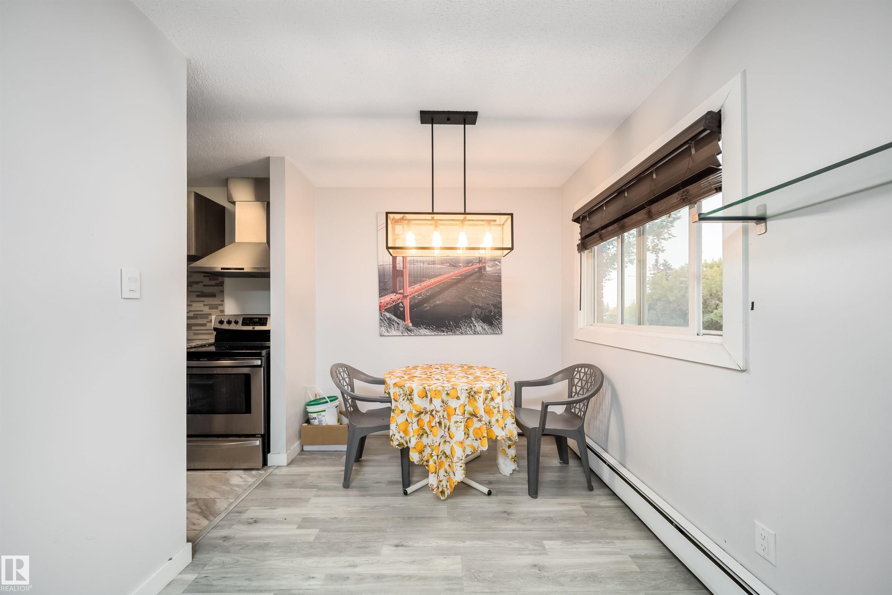 Wood-finish flooring, contemporary chandelier, bright window with blinds, and glass shelving - #202 10615 156 St Nw, Edmonton, AB