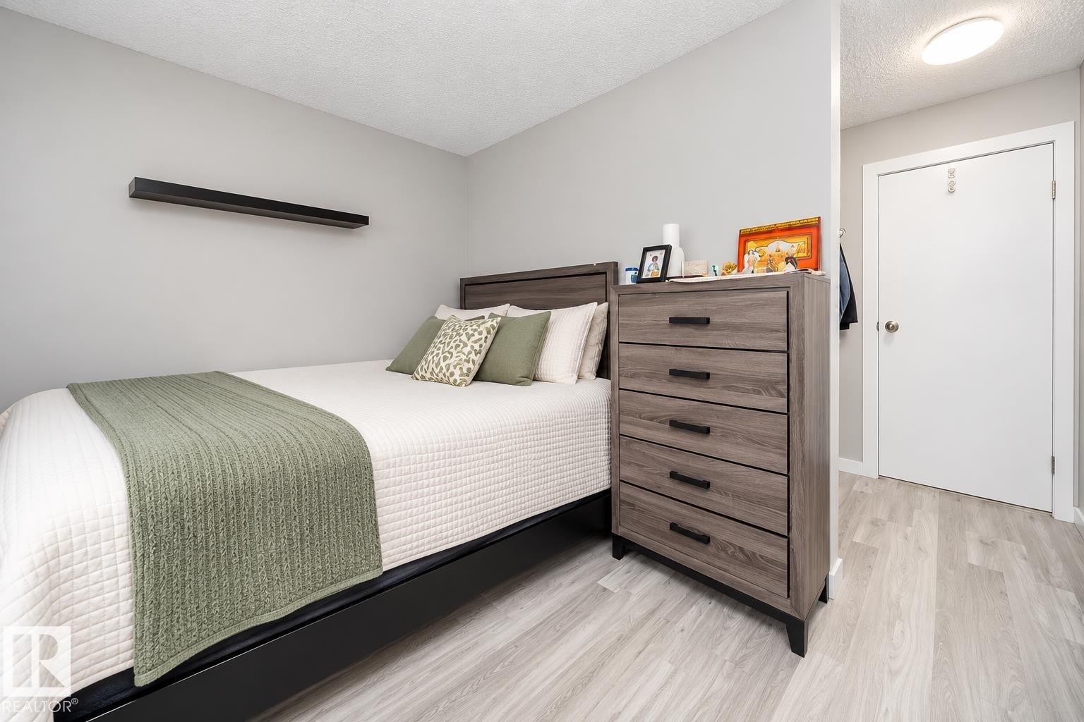 Light-toned wood-finish flooring, a contemporary floating shelf, and a built-in overhead light fixture - #202 10615 156 St Nw, Edmonton, AB