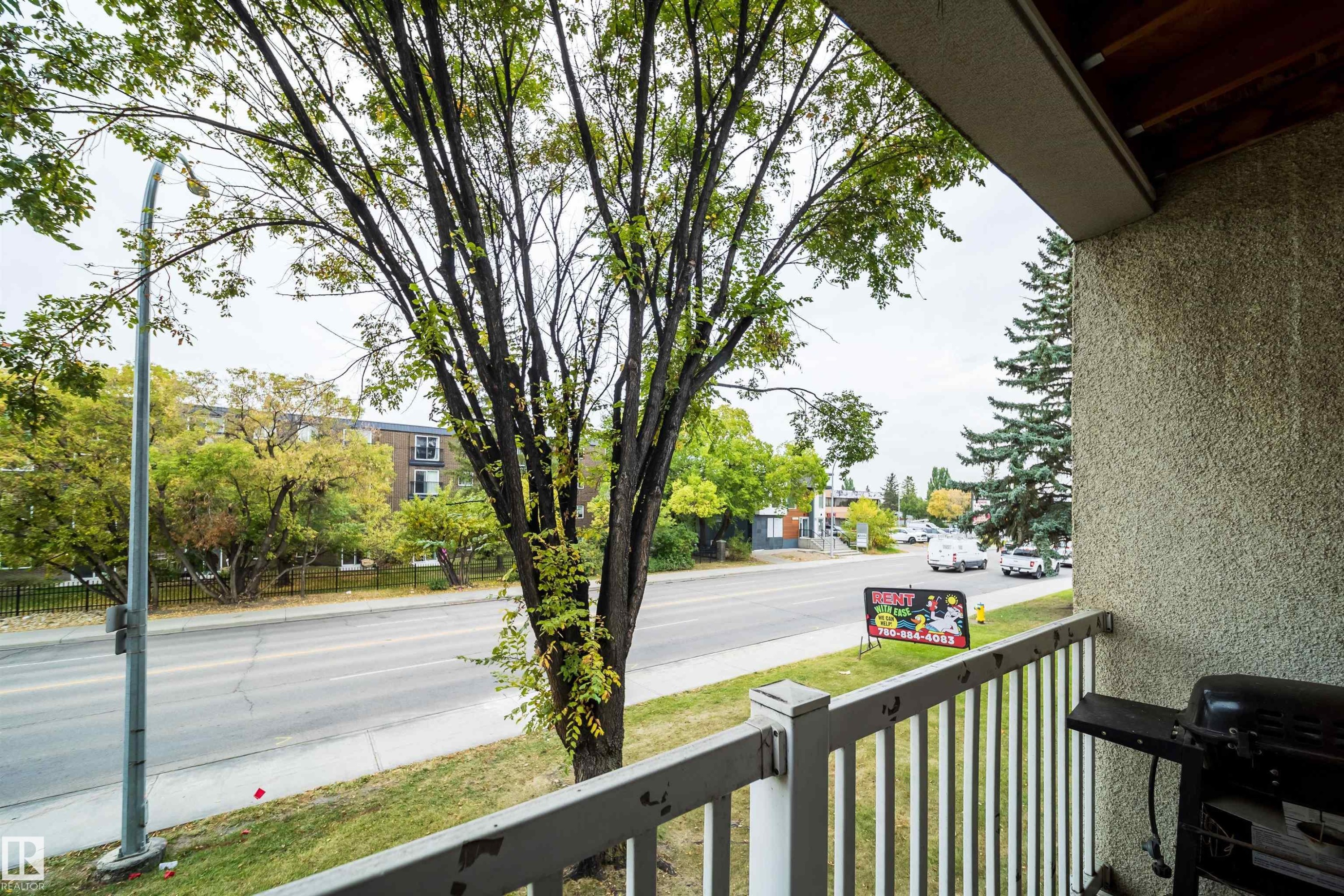 Balcony with textured exterior wall, white railing, and tree-lined streetscape - #202 10615 156 St Nw, Edmonton, AB
