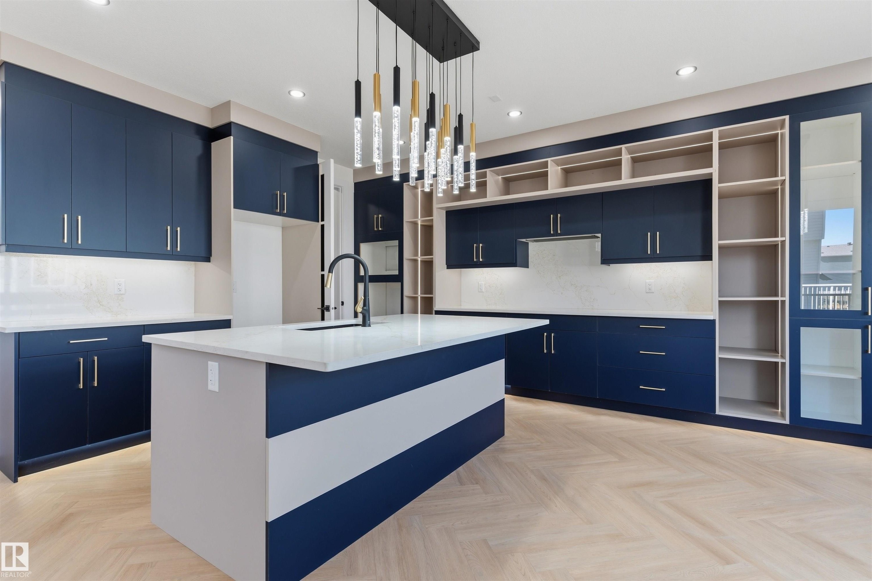 Kitchen featuring navy cabinetry, white countertops, a central island with an integrated sink, herringbone wood-finish flooring, and a linear pendant light fixture - 2720 63 Avenue, Rural Leduc County, AB