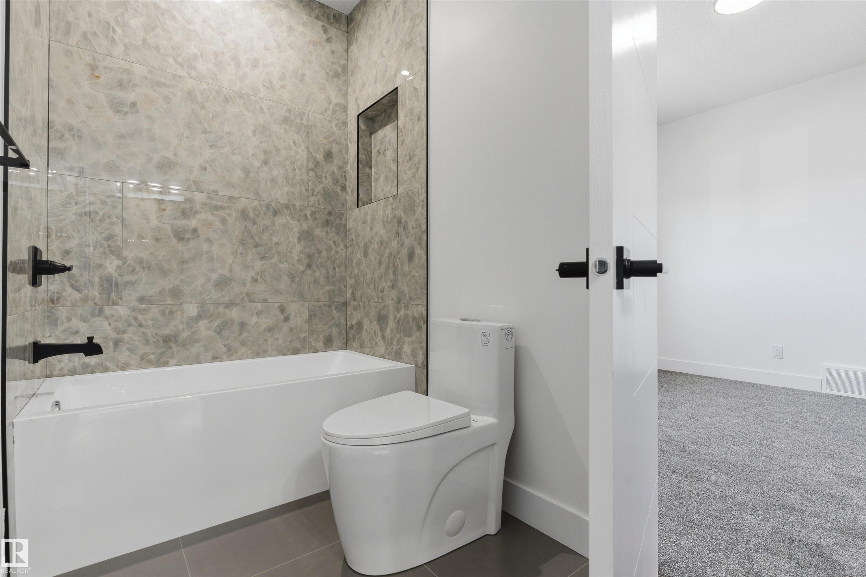 Bathtub with floor-to-ceiling marbled tile surround, featuring a recessed niche and matte black fixtures - 2720 63 Avenue, Rural Leduc County, AB
