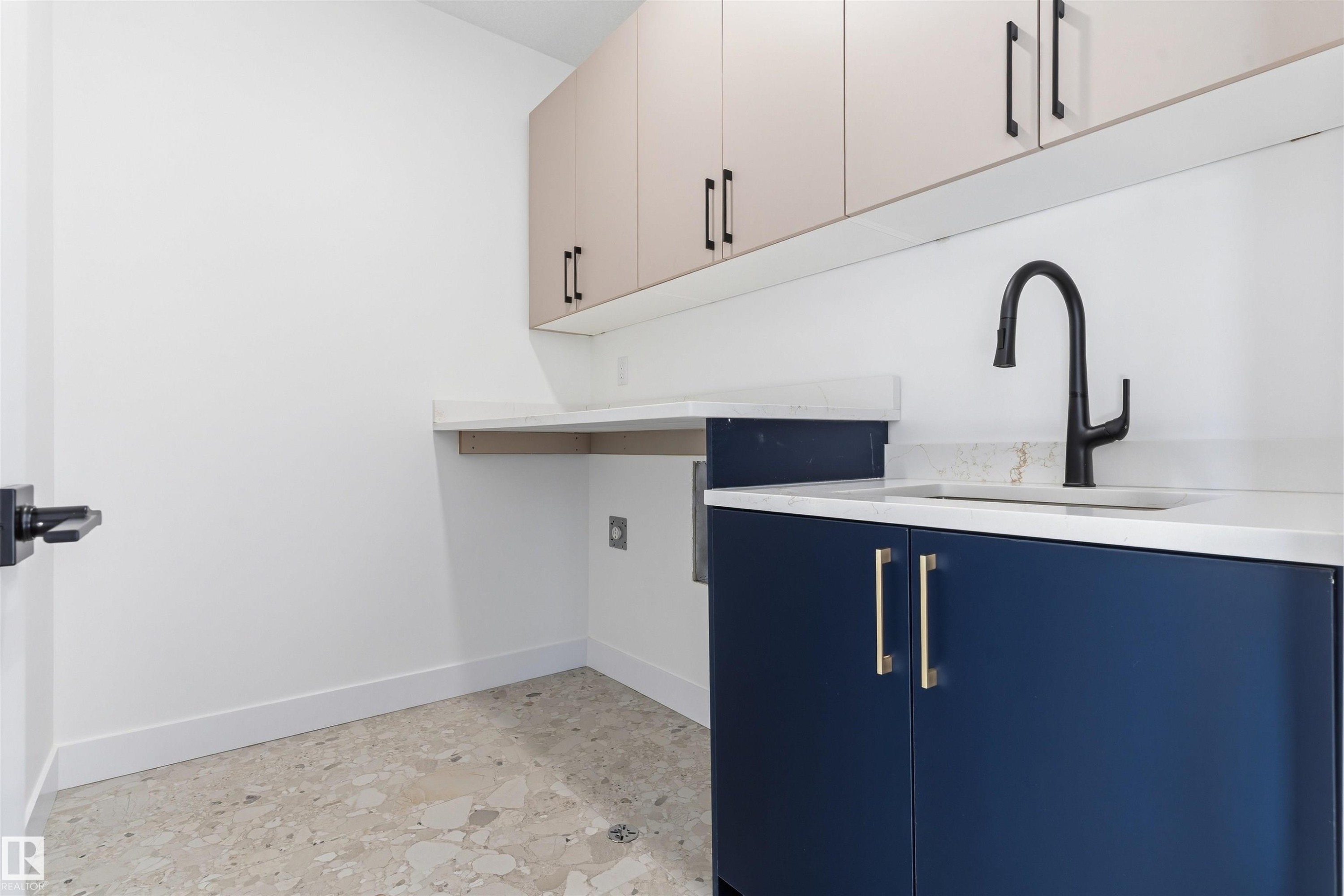 Built-in cabinetry with contrasting finishes, undermount sink, matte black gooseneck faucet, light-toned countertop, and terrazzo-style flooring - 2720 63 Avenue, Rural Leduc County, AB