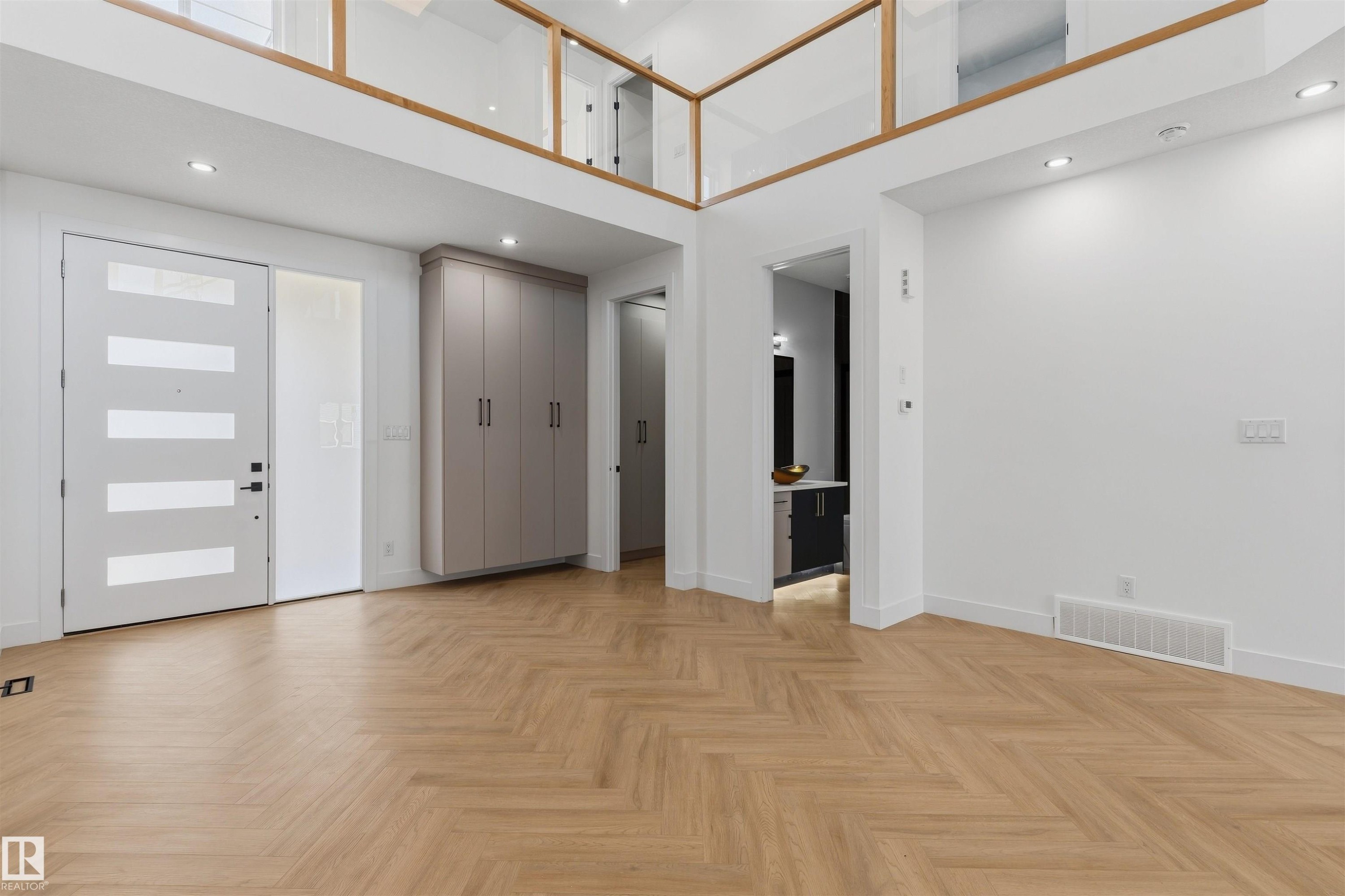 Herringbone wood-finish flooring, custom built-in cabinetry, modern entry door with frosted glass panels, recessed lighting, and a glass railing mezzanine - 2720 63 Avenue, Rural Leduc County, AB