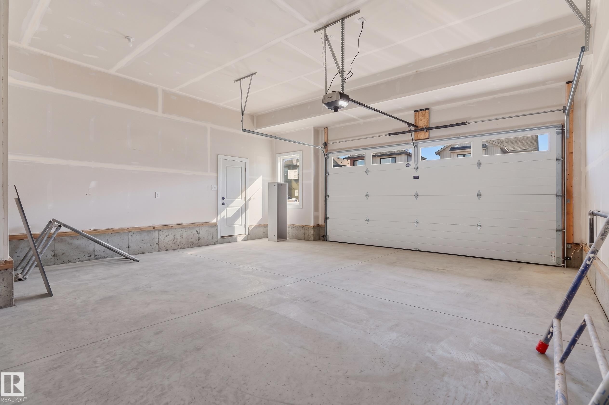 Spacious garage with exposed concrete flooring, white overhead garage door, built-in window, and interior access door - 2720 63 Avenue, Rural Leduc County, AB