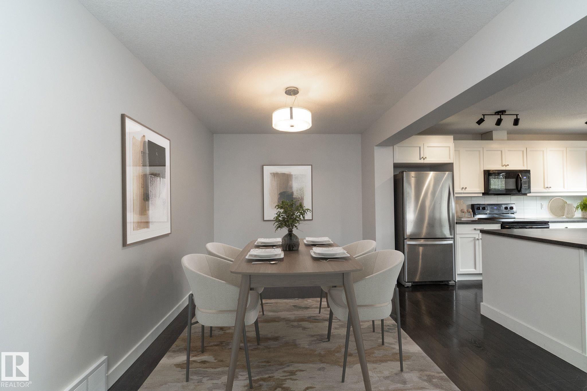 Recessed dining area with a contemporary chandelier, dark wood-finish flooring, and a kitchen featuring white cabinetry, dark countertops, and stainless steel appliances - 55 Michigan Street, Devon, AB