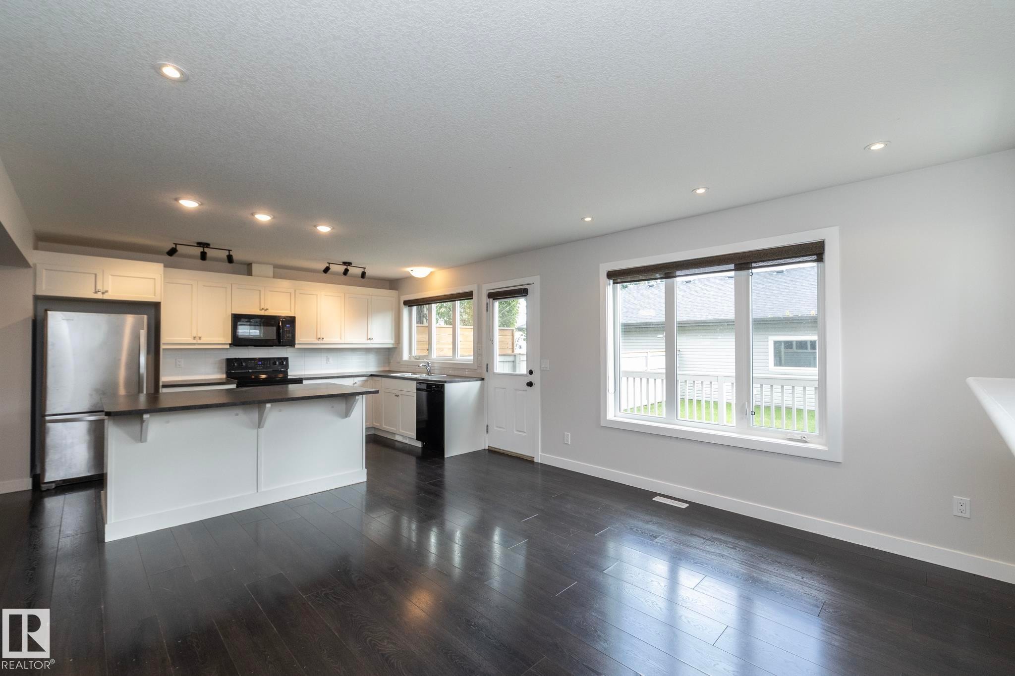 Open-concept living space with dark wood-finish flooring, recessed lighting, and a white kitchen featuring stainless steel appliances - 55 Michigan Street, Devon, AB