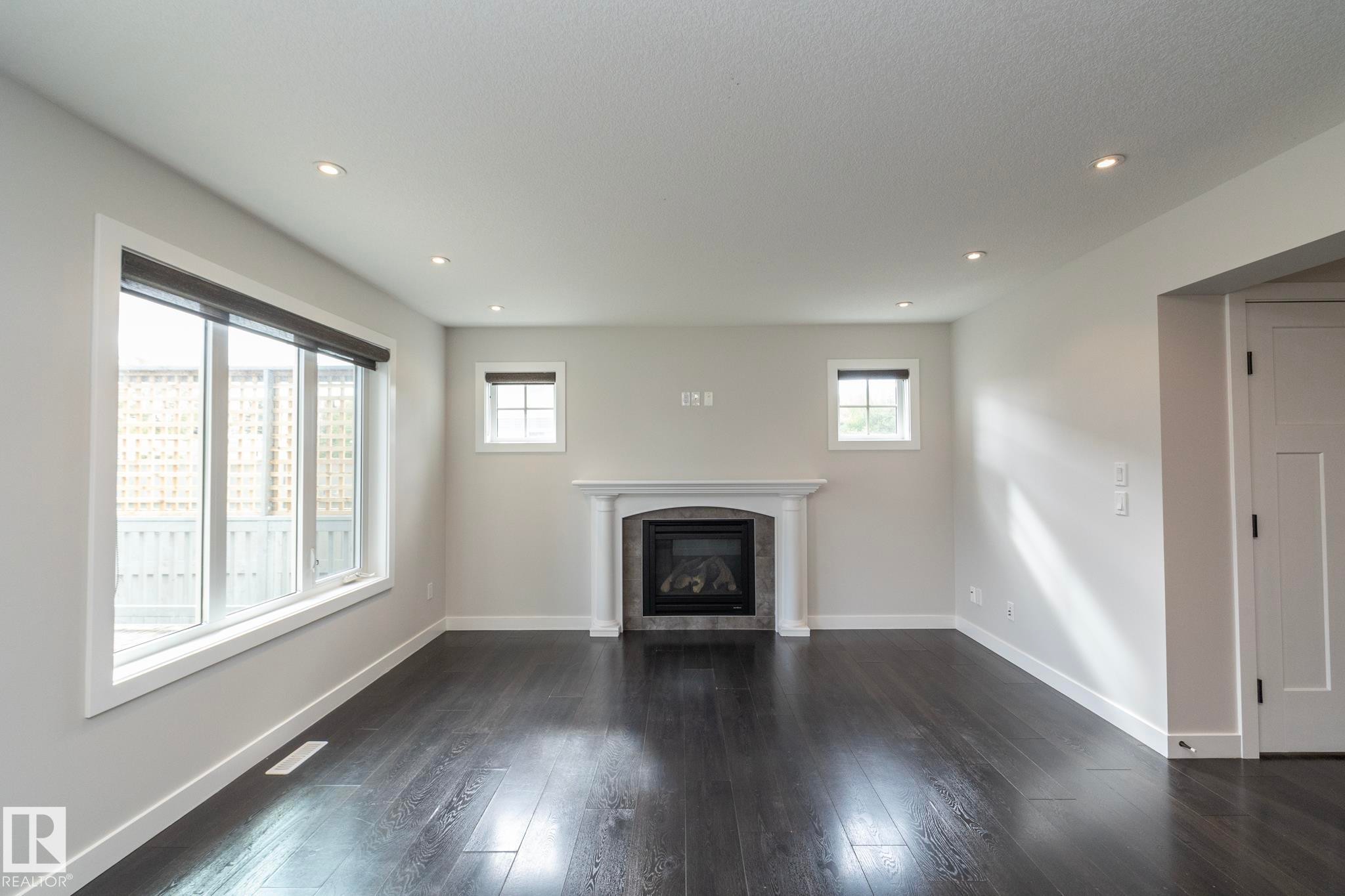 Dark wood-finish flooring, white trim, recessed lighting, and a fireplace with a white mantel and tile surround - 55 Michigan Street, Devon, AB