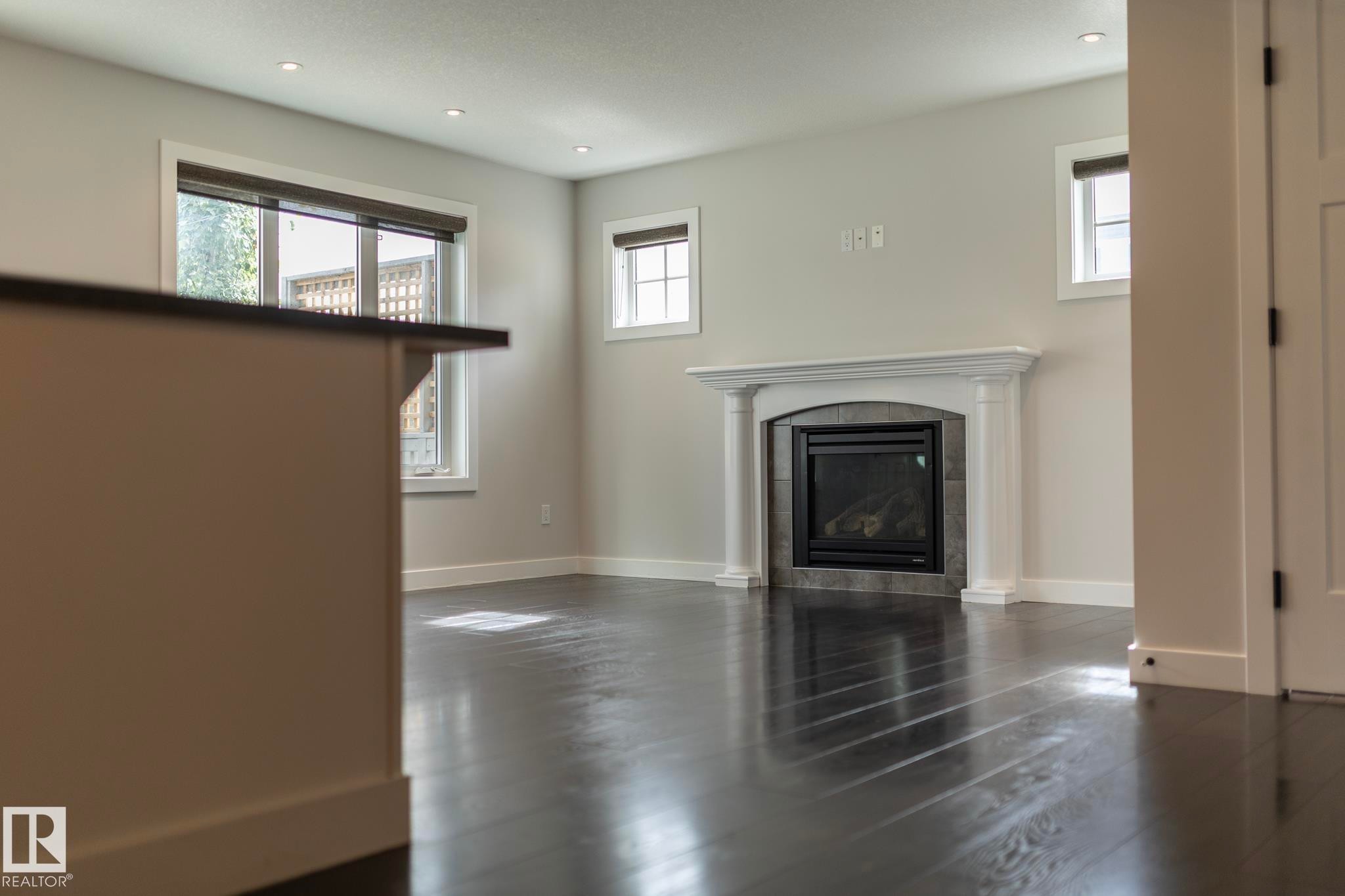 Dark wood-finish flooring, recessed lighting, and a fireplace with a decorative mantel and stone-tile surround - 55 Michigan Street, Devon, AB